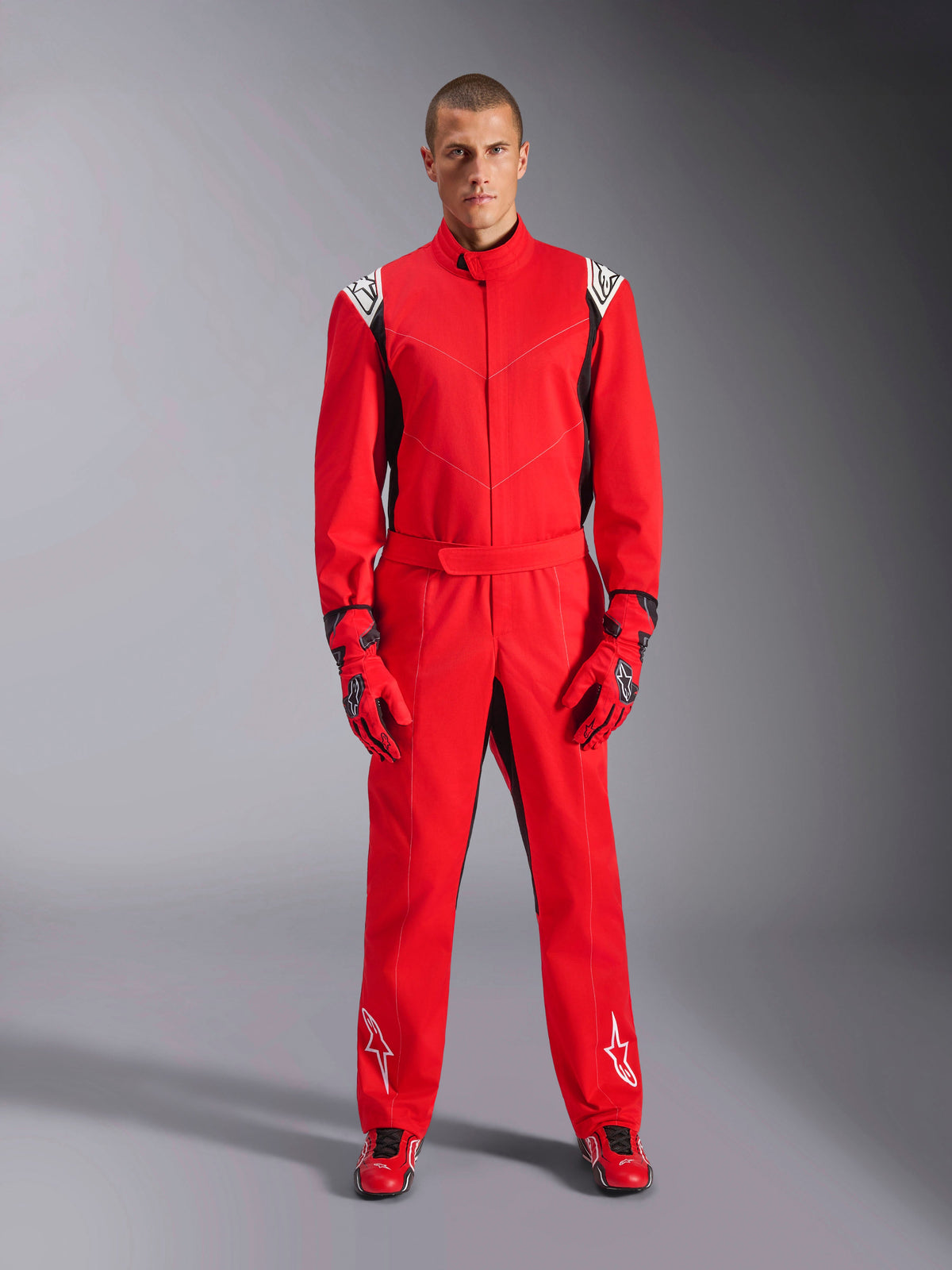 Combinaison Alpinestars Kart Indoor V2, rouge, combinaison de karting une pièce portée avec des gants et des chaussures de course rouges assortis, avec des logos blancs sur les épaules et les jambes, des accents noirs et un design profilé pour le karting récréatif.