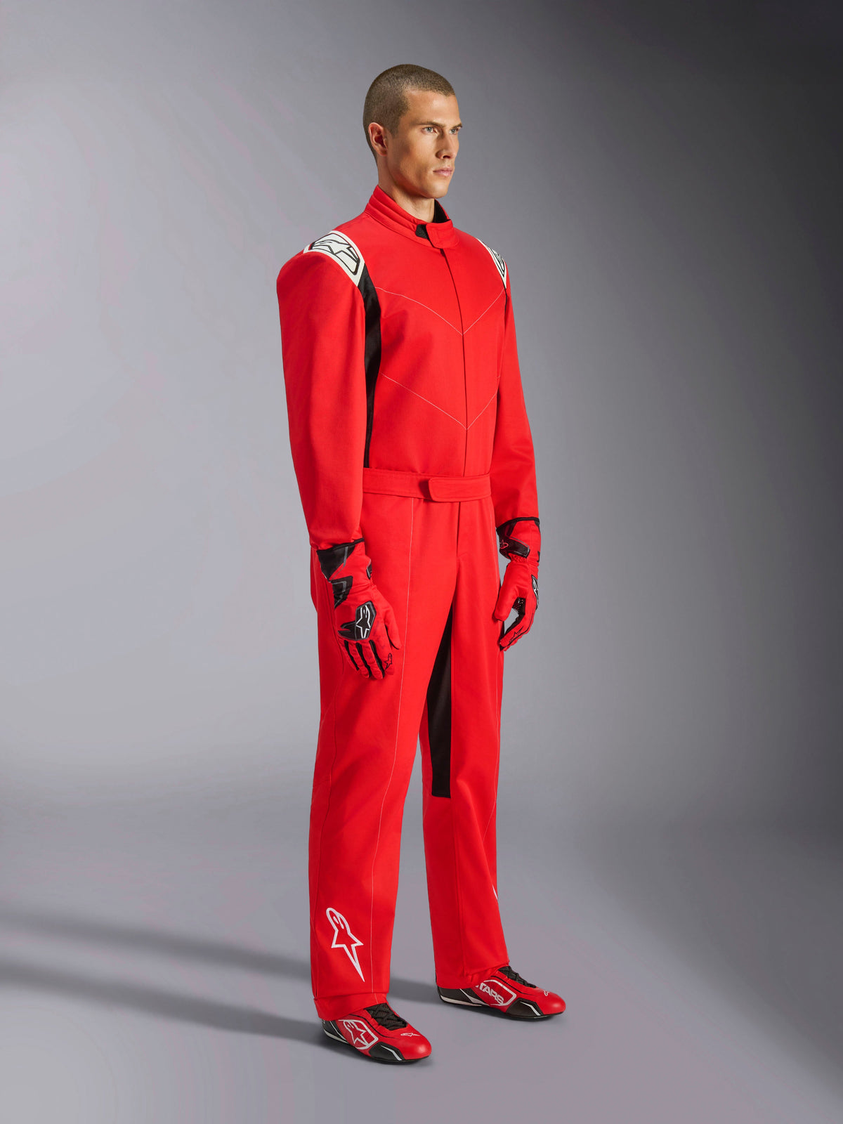 Combinaison Alpinestars Kart Indoor V2, combinaison de karting rouge, portée par un mannequin avec gants et chaussures assortis rouge et noir, avec logos blancs sur les épaules et le bas de la jambe, accents noirs, conçue pour le karting récréatif et les pistes intérieures