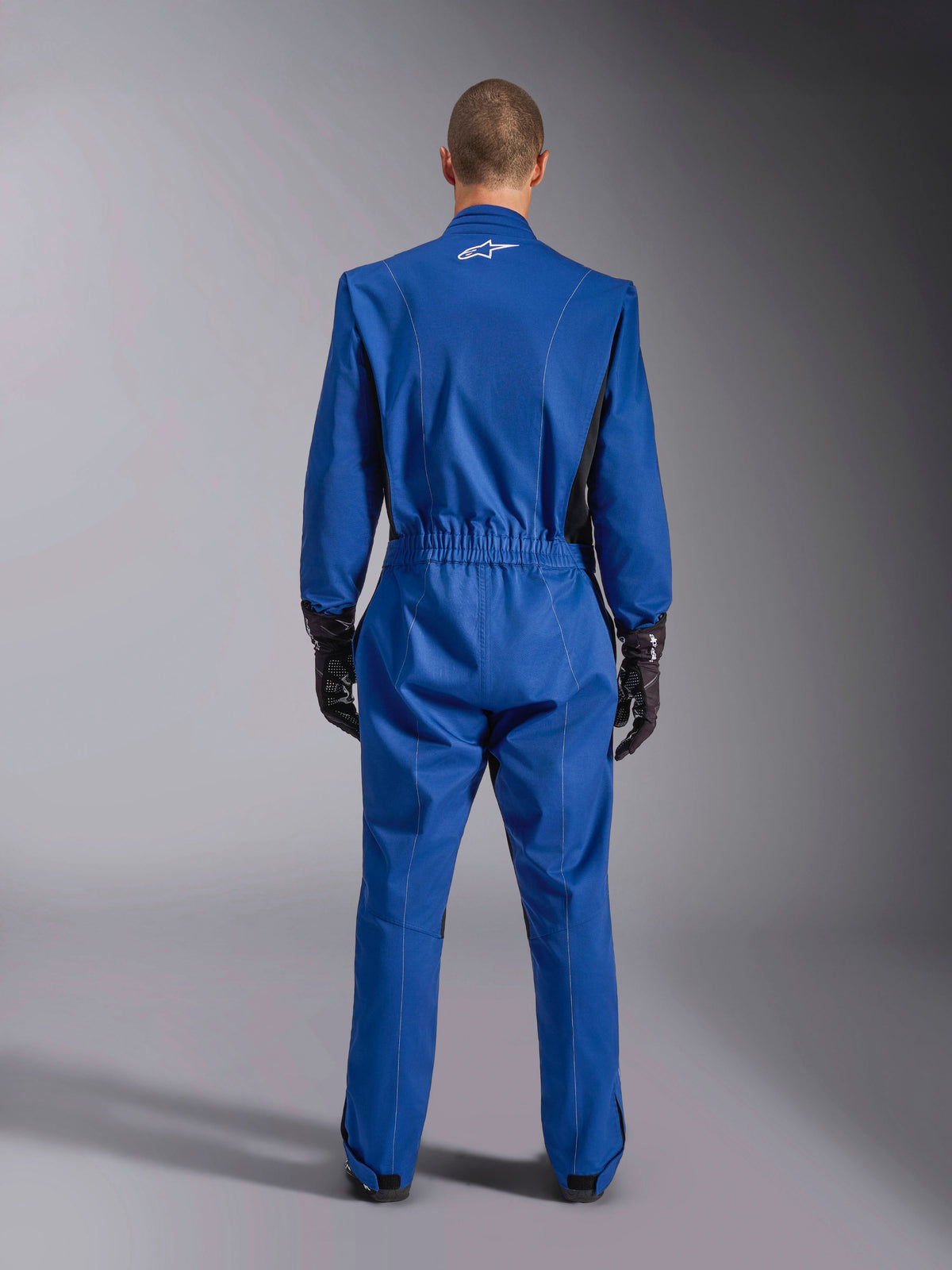 Combinaison Alpinestars Kart Indoor V2, bleue, vue de dos, combinaison de karting une pièce dotée d'un logo blanc sur le haut du dos, d'une taille élastiquée et d'accents noirs, portée avec des gants de course noirs