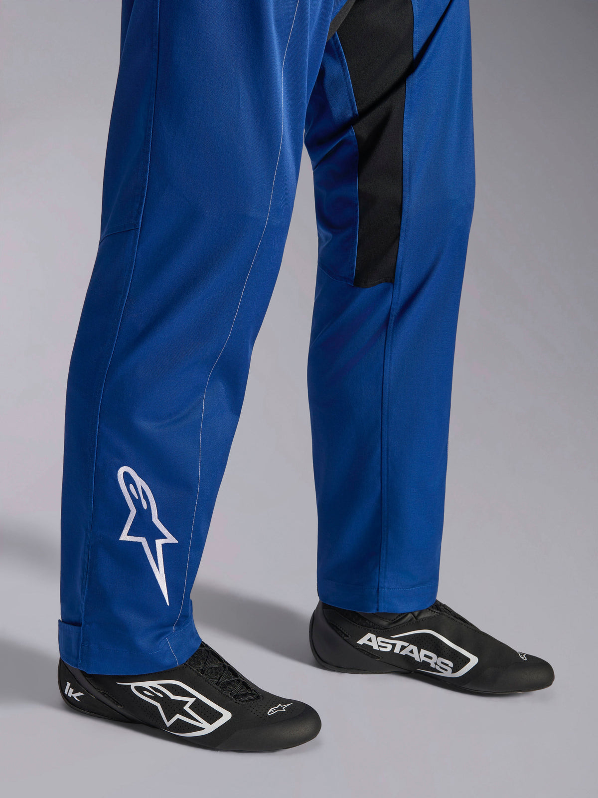 Combinaison Kart Indoor V2 Alpinestars, bleue, gros plan sur le bas des jambes et les pieds montrant le logo étoile blanc sur la cheville, bas de jambe ajustables et chaussures de course noires, vêtement de karting durable pour une utilisation de loisir sur piste