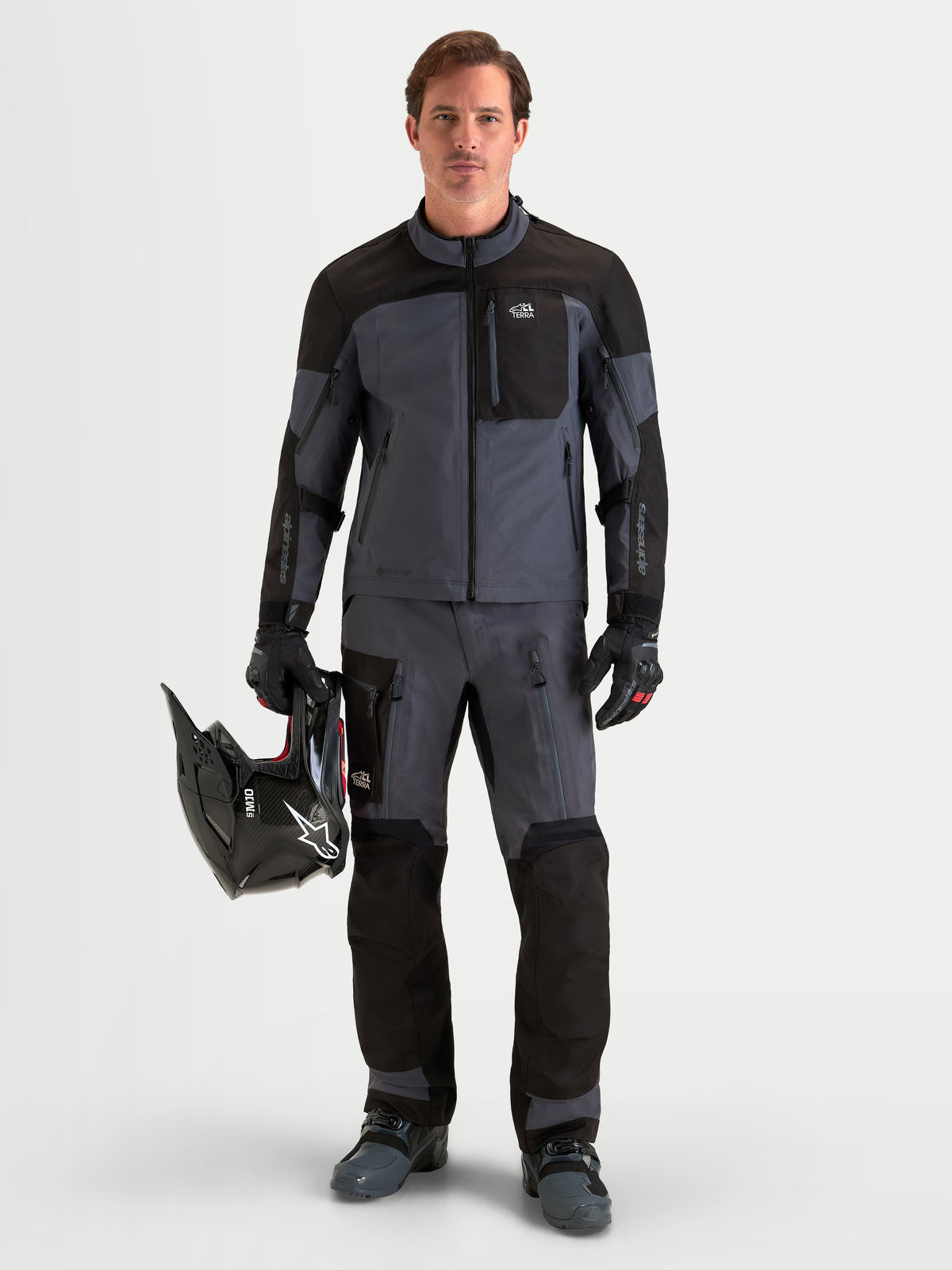 Alpinestars Tenue complète Arenis Gore-Tex, tenue complète de moto adventure pour homme noire et gris foncé, vue de face d'un modèle debout tenant un casque et portant un équipement de conduite étanche assorti