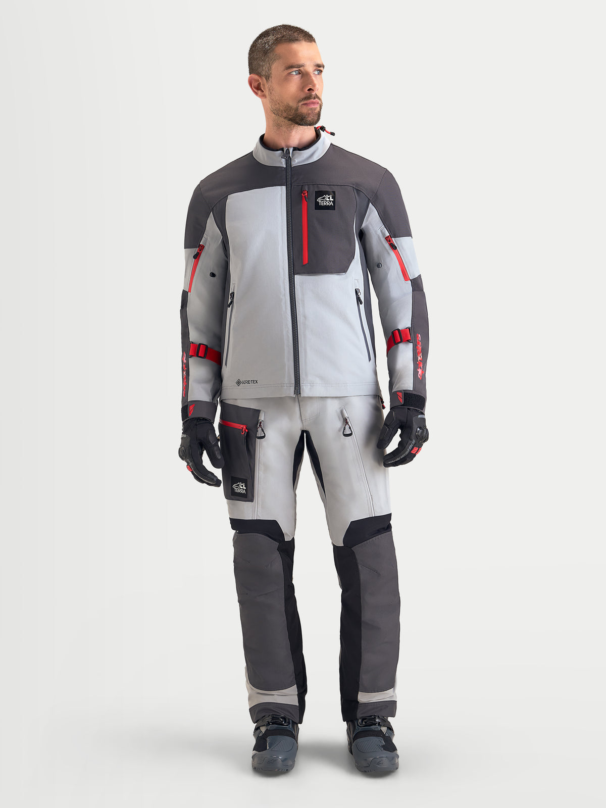 Alpinestars Arenis Gore-Tex Veste, veste de moto adventure pour homme gris moyen, gris foncé et noir, portée par un modèle avec des détails de zips rouges et une construction imperméable