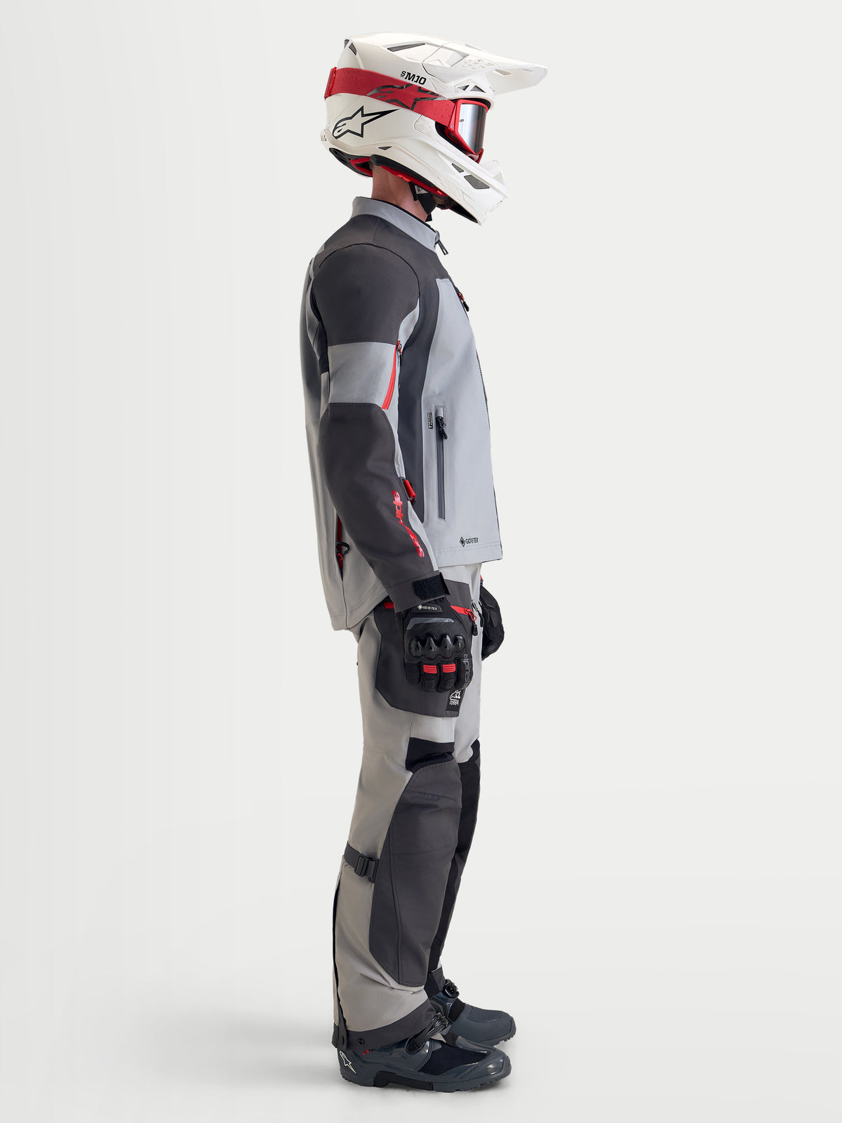 Alpinestars Arenis Gore-Tex Veste, veste de moto adventure pour homme en gris moyen, gris foncé et noir, vue de profil d'un pilote portant la veste textile imperméable avec un équipement assorti et un casque blanc et rouge