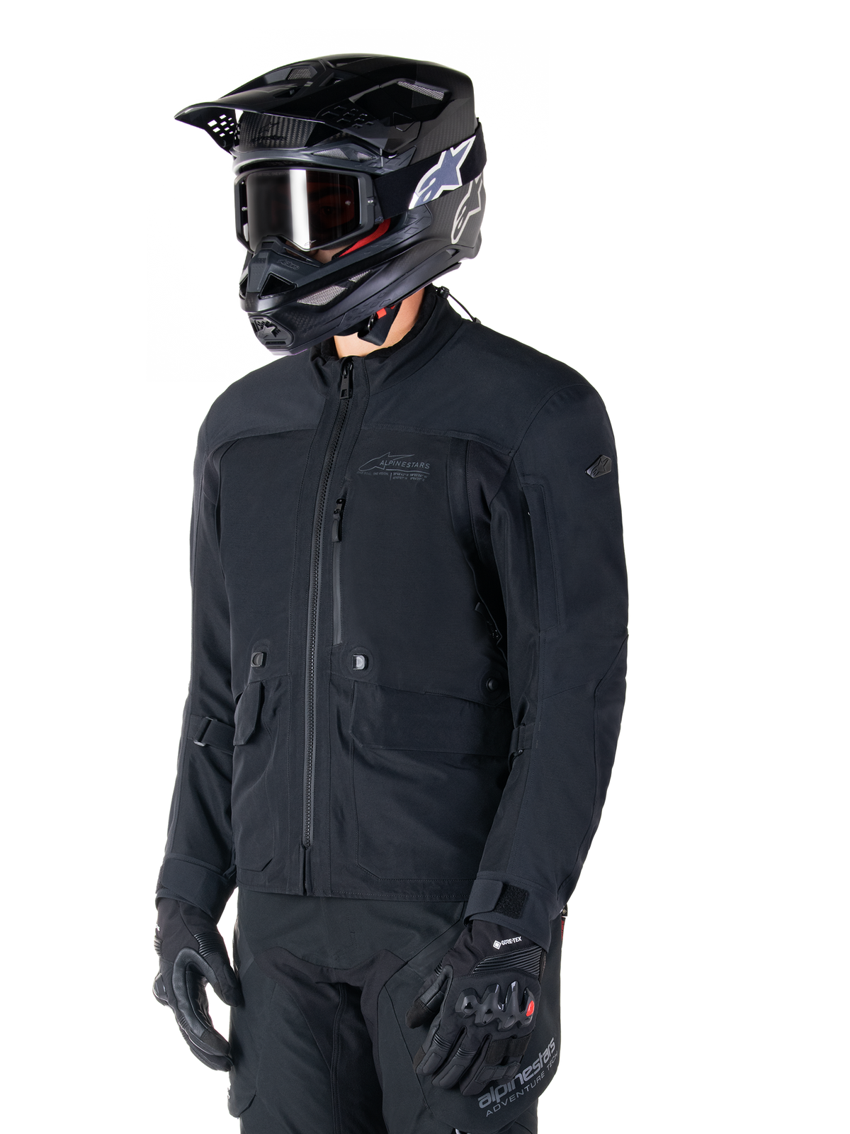 Alpinestars St-7 Prime GORE-TEX Jacket, Black motorcycle jacket, worn by a rider with a black helmet and goggles, featuring large chest cargo pockets and a laminated waterproof shell, premium adventure touring and commuting gear.