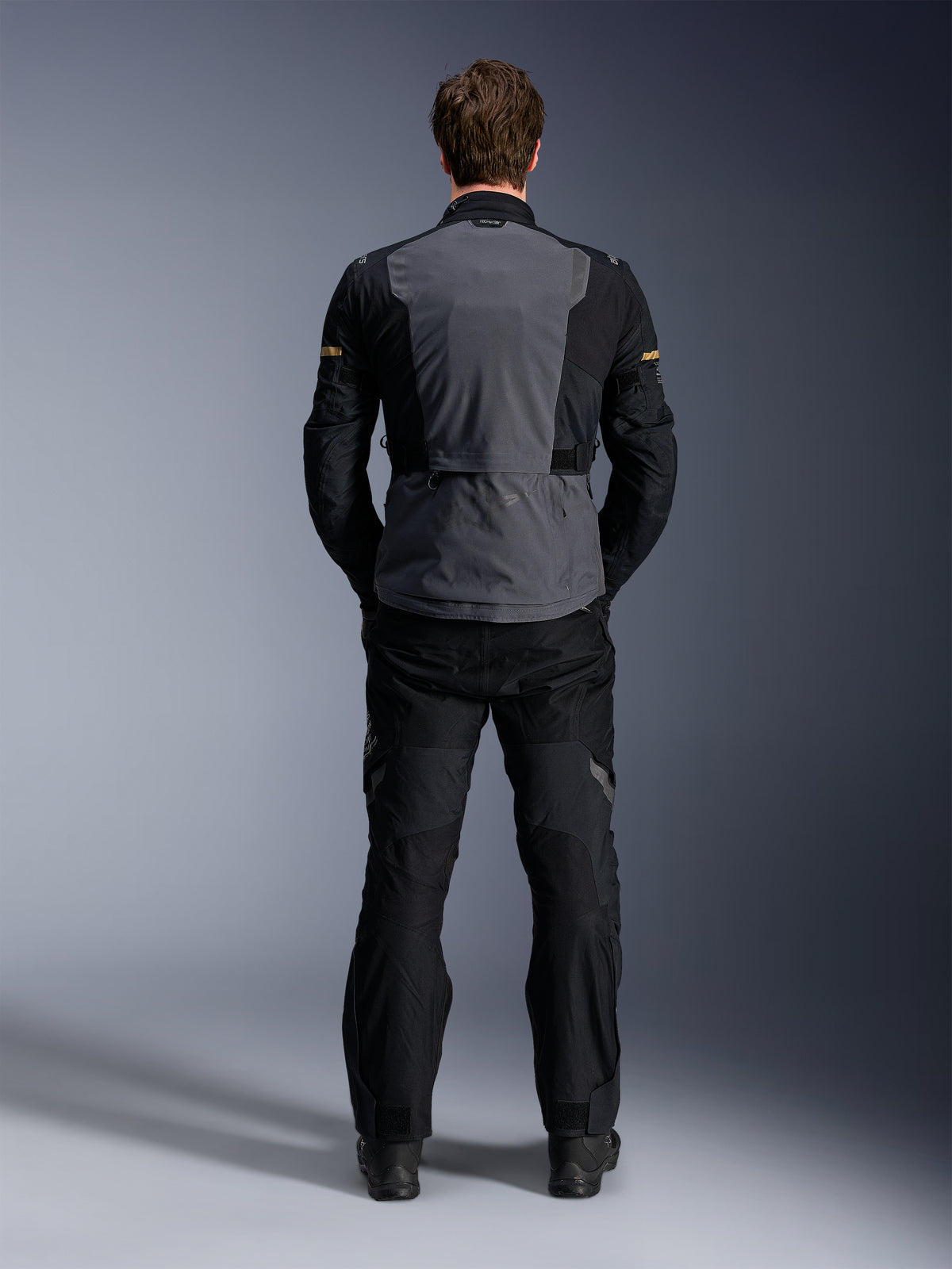 Veste Alpinestars ST-7 2L GORE-TEX, Gris Foncé Noir et Kaki Foncé, vue arrière sur un modèle, veste de moto adventure touring avec panneau arrière gris et manches articulées noires, portée avec un pantalon noir assorti