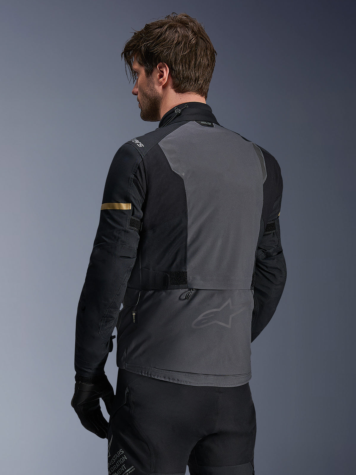 Veste Alpinestars ST-7 2L GORE-TEX, veste de moto, gris foncé, noir et kaki foncé, vue arrière montrant un large panneau dorsal gris avec un logo discret, manches noires avec des accents kaki dorés, conception textile imperméable prête pour l'aventure.