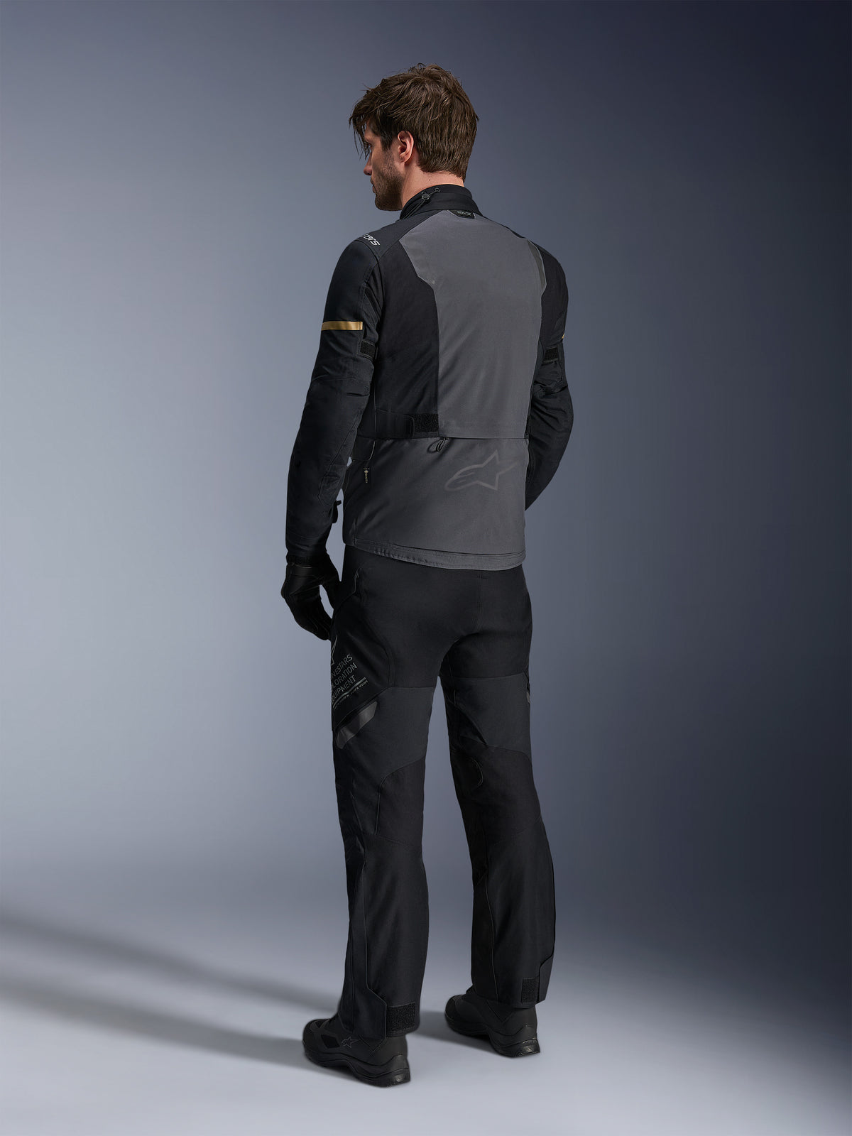 Veste Alpinestars ST-7 2L GORE-TEX, gris foncé et noir avec accents kaki foncé, vue arrière d'un motard portant la veste et le pantalon de moto assortis, équipement de touring aventure avec construction laminée imperméable