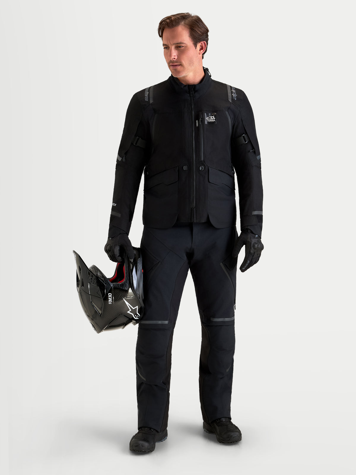 Alpinestars St-7 V2 2L Gore-Tex Pantalons Short, pantalon de moto adventure pour homme noir, vue de face sur un modèle portant un équipement assorti et tenant un casque, vêtement de conduite tout-terrain imperméable certifié AA