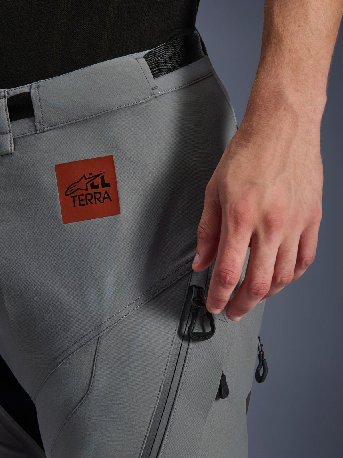 Alpinestars Nazca 3L GORE-TEX PRO Pants, Adventure Motorcycle Pants, Dark Gray, close-up of upper thigh featuring a reddish-brown All Terra logo patch, zippered cargo pocket with black pulls, durable textile construction for all-terrain riding