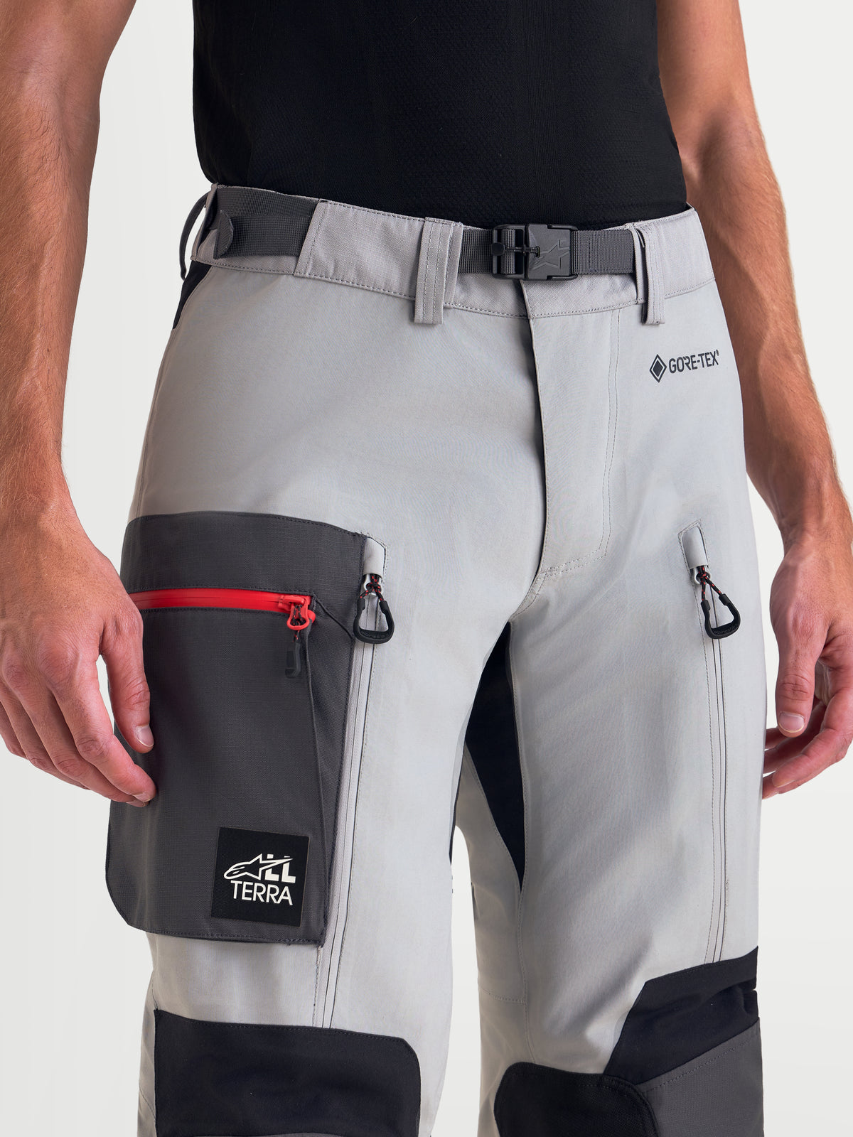 Alpinestars Arenis Gore-Tex Pantalons, pantalon de moto adventure pour homme en gris moyen, gris foncé et noir, vue rapprochée montrant la boucle magnétique à la taille, le logo GORE-TEX, les ventilations zippées sur les cuisses et la poche cargo porté par un modèle