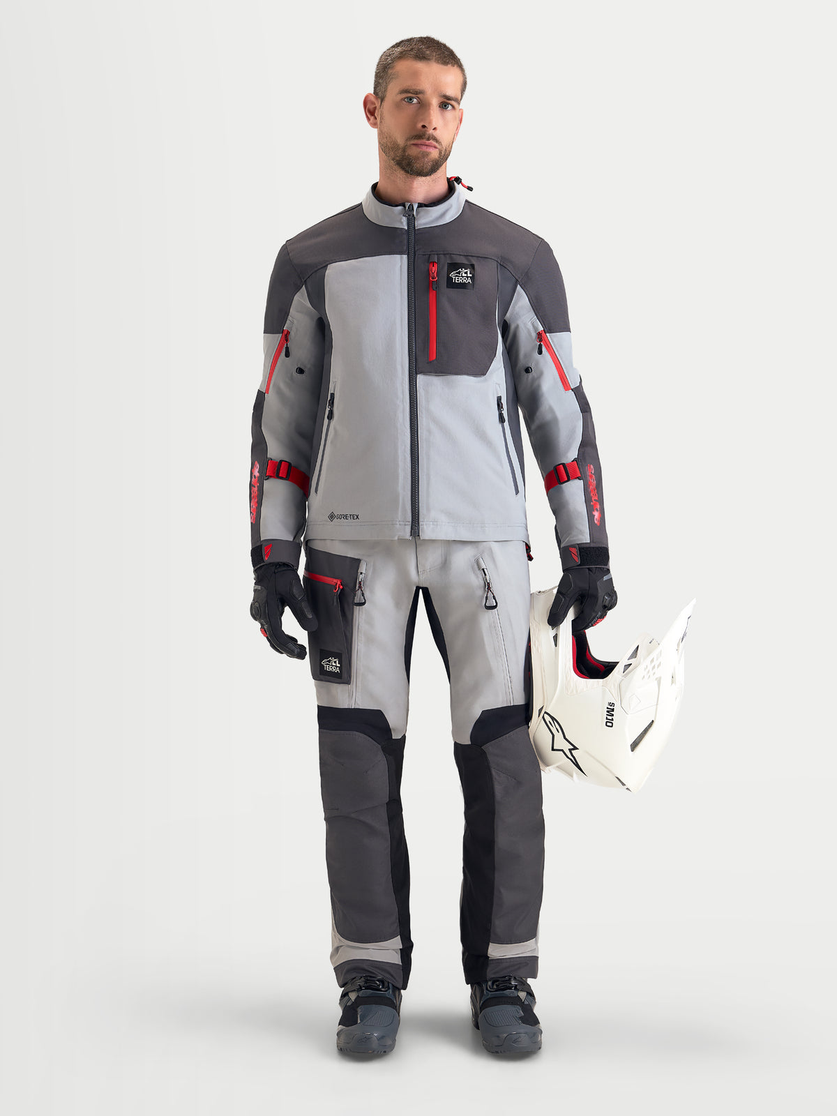 Alpinestars Arenis Gore-Tex Pantalons, pantalon de moto adventure pour homme en gris, gris foncé et noir, vue de face sur un modèle portant une veste assortie et tenant un casque