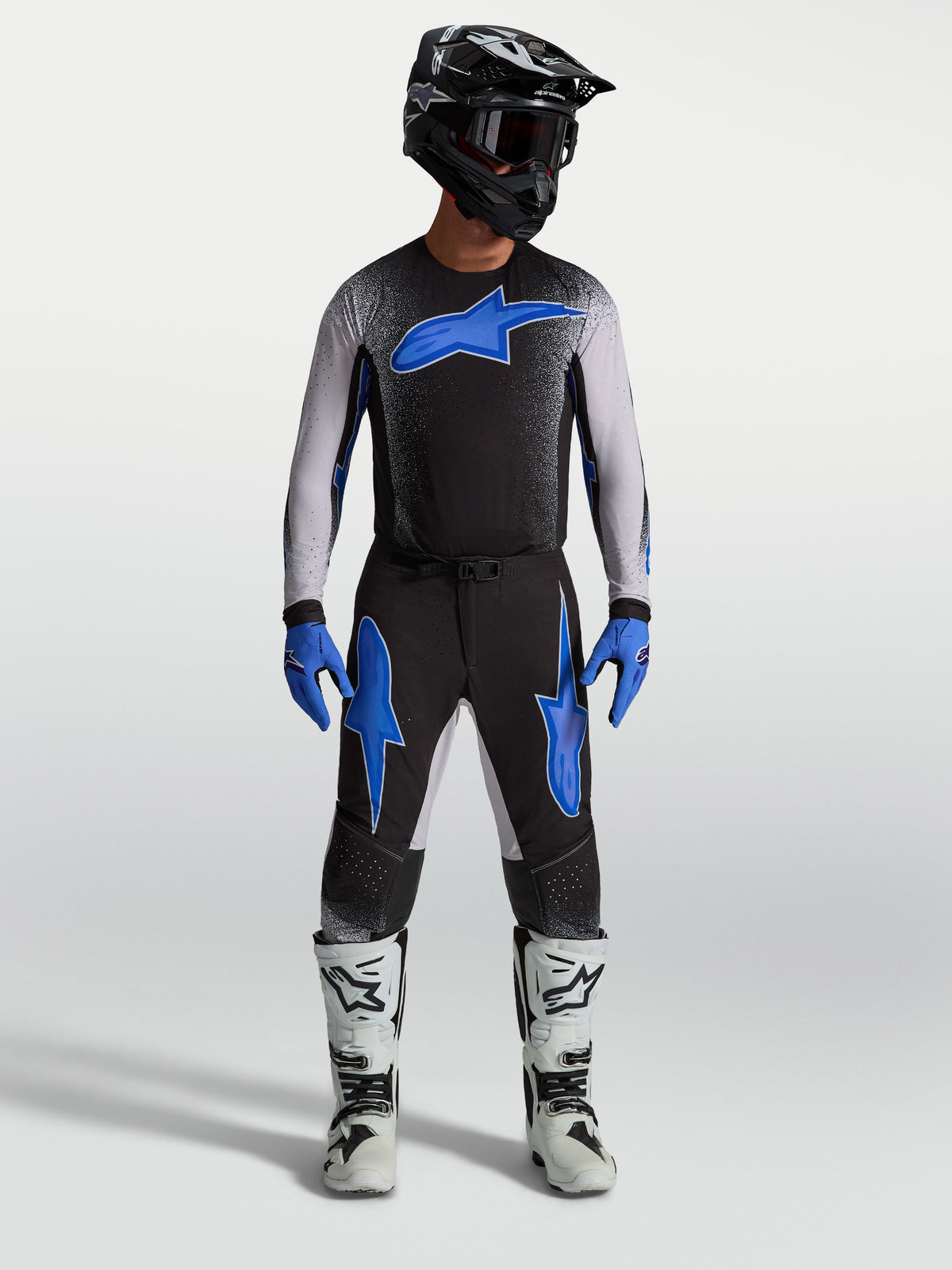 Pantalons Alpinestars Supertech Hiten AFD, équipement de motocross noirs et bleus, portés par un mannequin avec un maillot assorti et des bottes blanches, style performance tout-terrain.