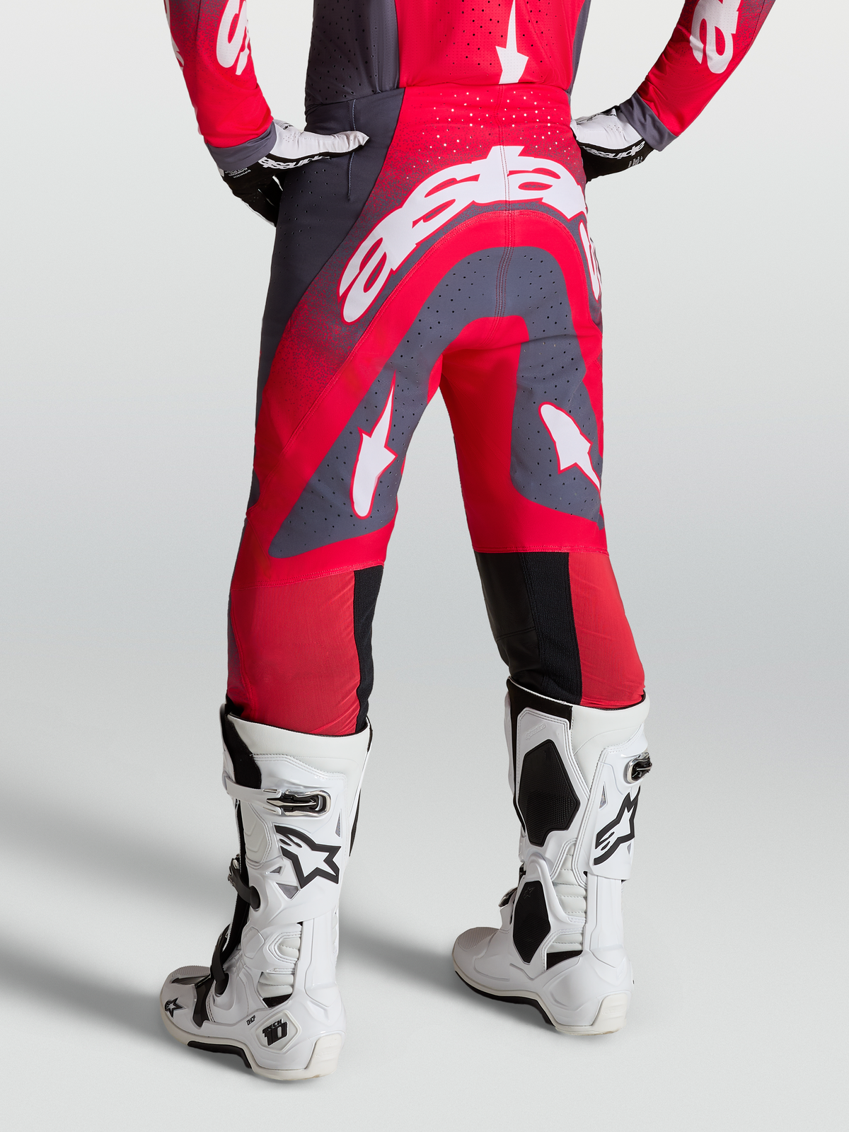 Alpinestars Supertech Hiten AFD, pantalon de motocross rouge et gris, vue arrière sur mannequin avec bottes de course blanches, coupe athlétique pro racing.