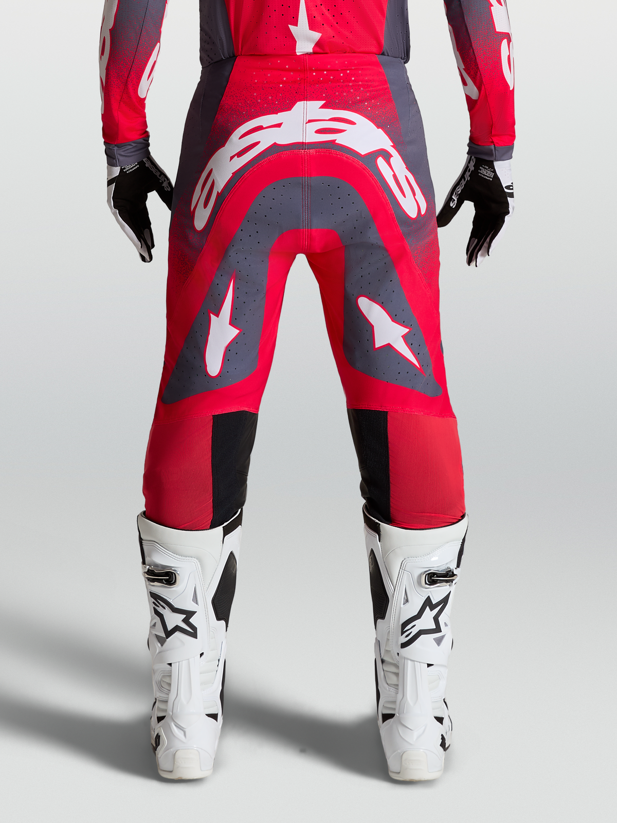 Alpinestars Supertech Hiten AFD, pantalon de motocross professionnel pour homme, rouge fluo et gris avec logos blancs, vue de dos montrant la coupe athlétique et les zones perforées pour la ventilation.