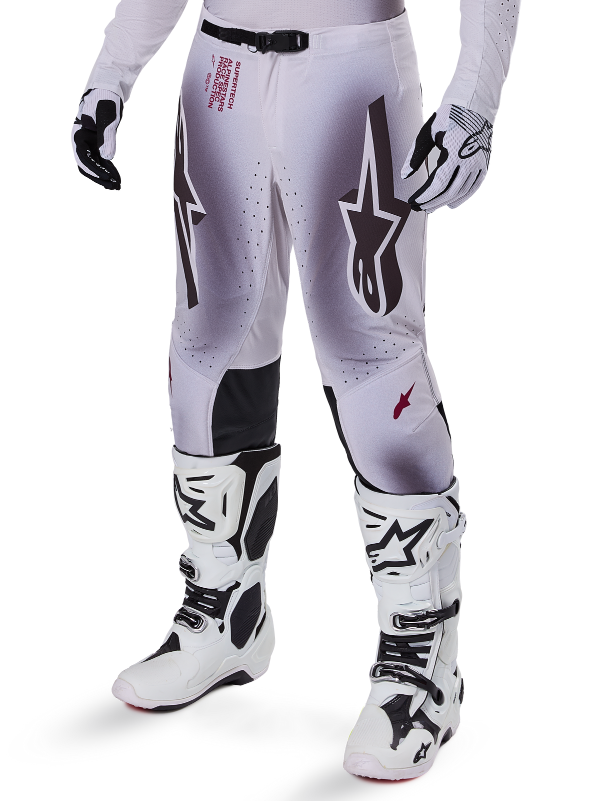 Alpinestars Pantalon Supertech Maker 2025, pantalon de motocross, argent et noir, avec de grands logos étoiles et un lettrage rouge, présenté avec des bottes et des gants blancs assortis