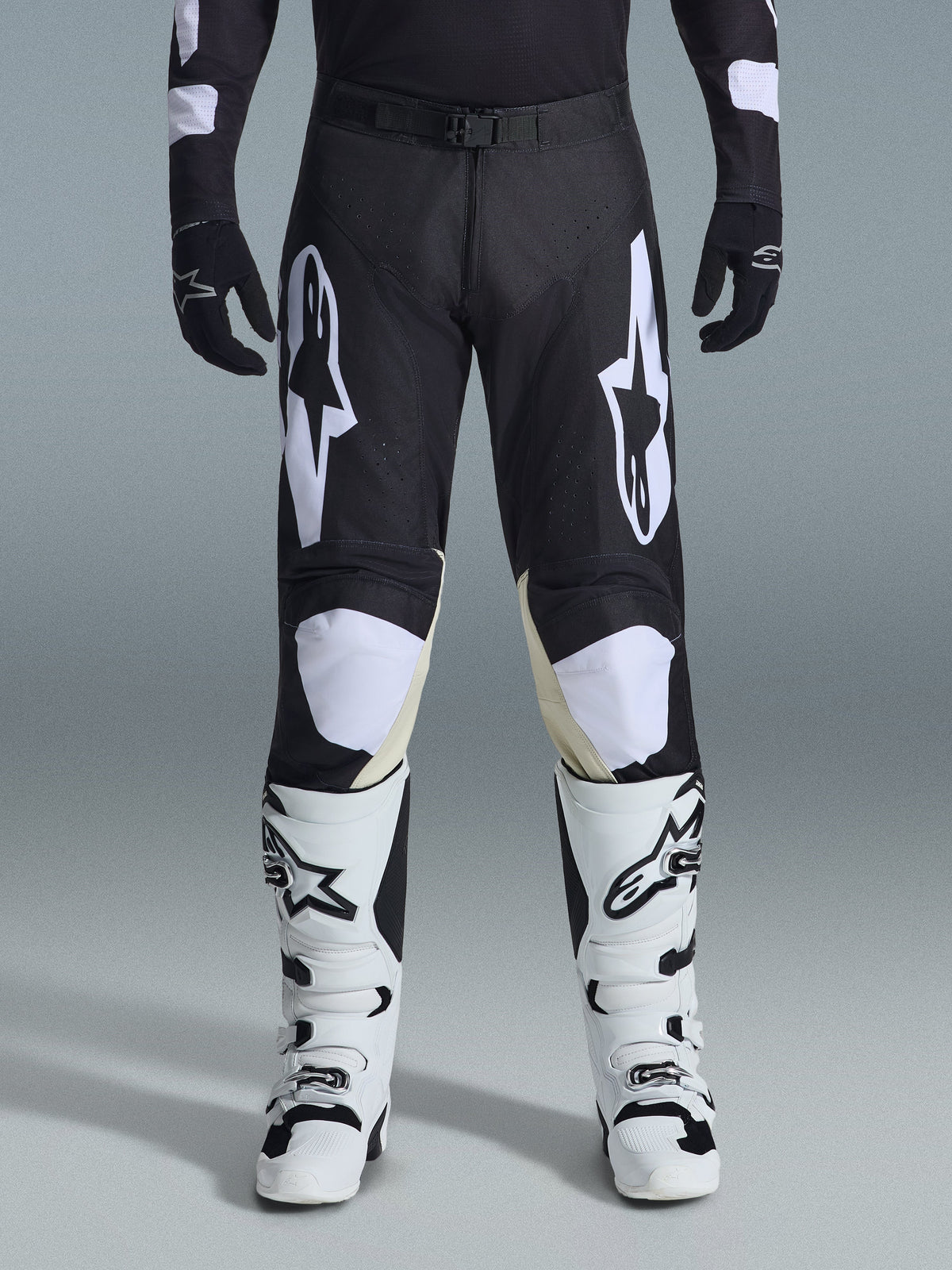 Pantalon Alpinestars Racer Air Riway 2026, pantalon de motocross, noir et blanc, avec des logos Alpinestars blancs sur les cuisses et les genoux, associé à des bottes de motocross blanches et noires et des gants noirs, coupe de course athlétique pour le pilotage tout-terrain