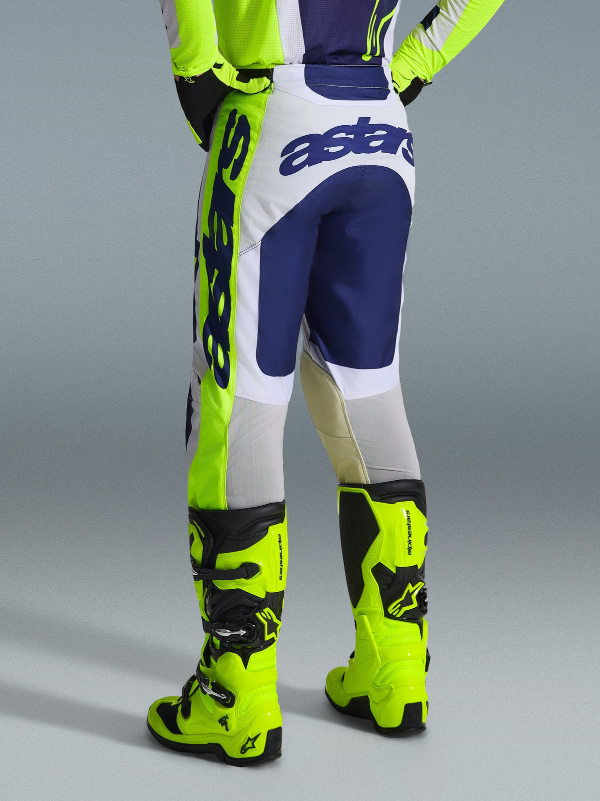 Pantalon Alpinestars Racer Air Riway 2026, pantalon de motocross, gris clair, jaune fluo et bleu, vue arrière montrant le logo « astars » sur l'assise et le côté, porté avec des bottes de motocross jaune fluo assorties, coupe athlétique de course conçue pour la performance tout-terrain