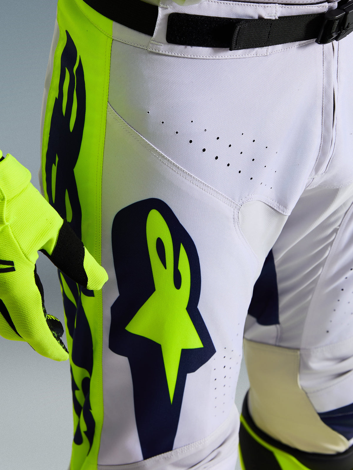 Pantalon Alpinestars Racer Air Riway 2026, gros plan sur un pantalon de motocross blanc et bleu marine avec empiècements jaune vif, doté de perforations de ventilation découpées au laser et du logo Astar distinctif, associé à un gant jaune assorti