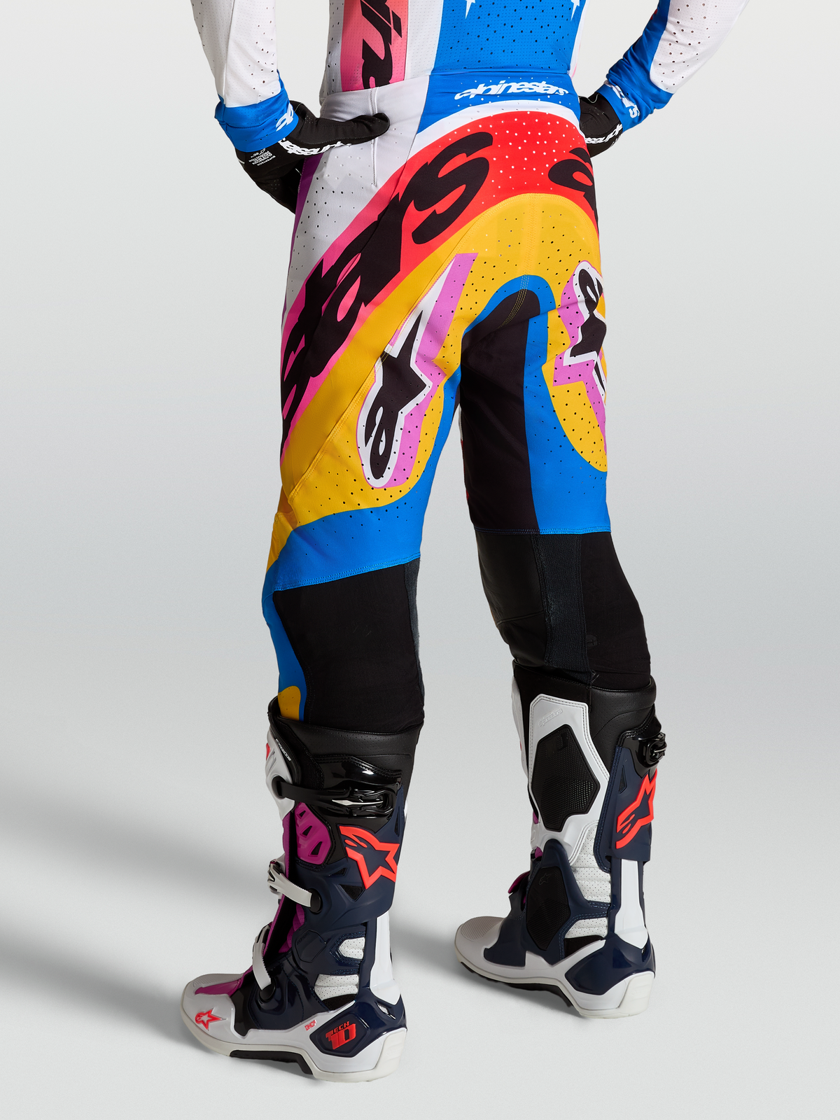 Pantalons Supertech Dyna d'Alpinestars, pantalons de motocross de course en blanc et bleu, portés par un mannequin, dotés de panneaux ventilés et d'une coupe athlétique pour la performance.