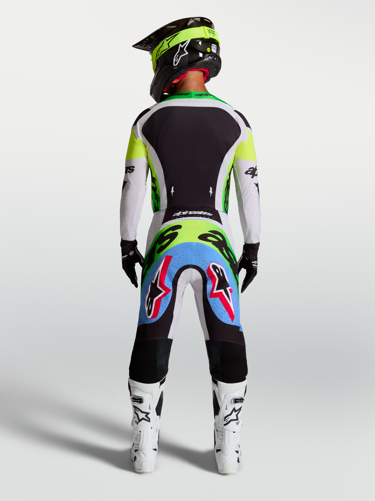 Pantalon Alpinestars Supertech Dyna, pantalon de motocross lilas et vert fluo, vue arrière d'un pilote en kit de course.