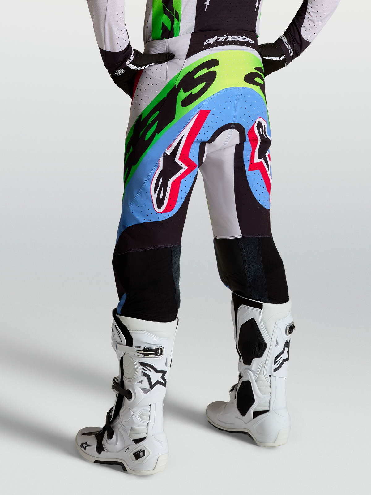 Alpinestars Pantalon Supertech Dyna, pantalon de motocross pour homme, lilas clair et vert fluo, porté par un pilote avec des bottes blanches, tissu rip-stop perforé et genoux en cuir de chèvre