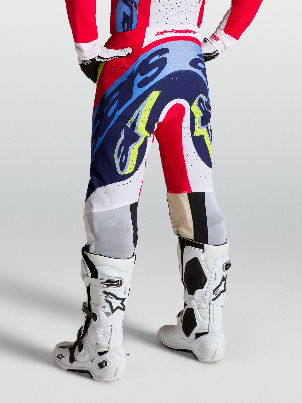 Alpinestars Pantalon Supertech Dyna, pantalon de motocross rouge, blanc et bleu marine, coupe athlétique racing portée par un mannequin avec des bottes blanches, équipement de protection tout-terrain haute performance