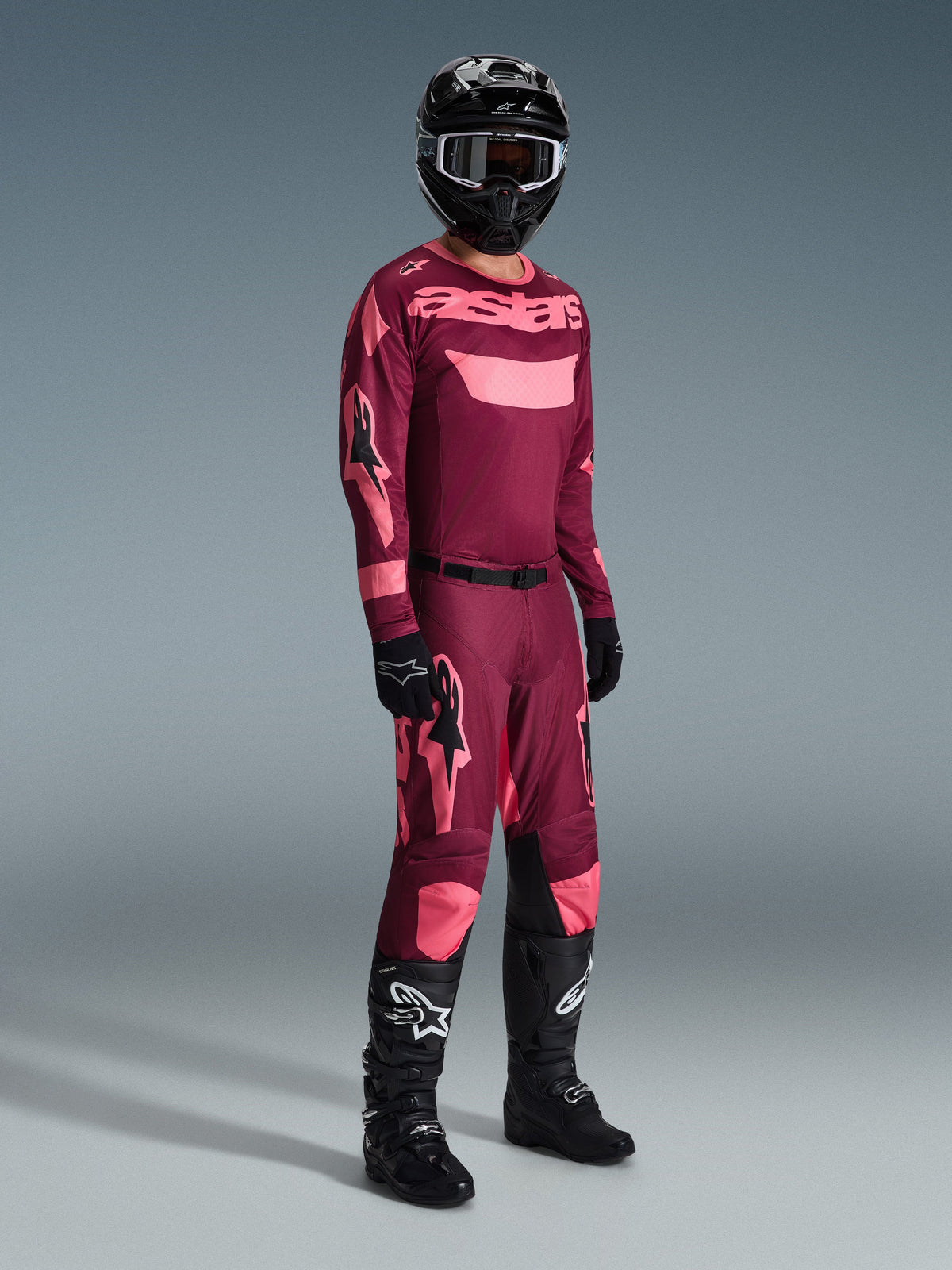 Ensemble d'équipement Alpinestars Racer Riway 2026, maillot et pantalon de motocross bordeaux et rose, porté avec un casque noir et des bottes noires de la série Tech, vue en pied sur fond gris.