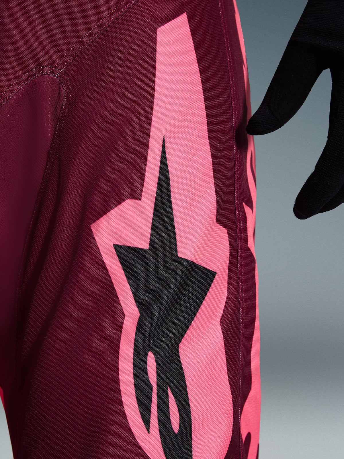 Pantalon Alpinestars 2026 Racer Riway, pantalon de motocross, Dark Red Coral, gros plan montrant un large graphisme angulaire rose corail et le logo étoile noir, mettant en avant la texture durable en poly-tissu et les coutures de performance