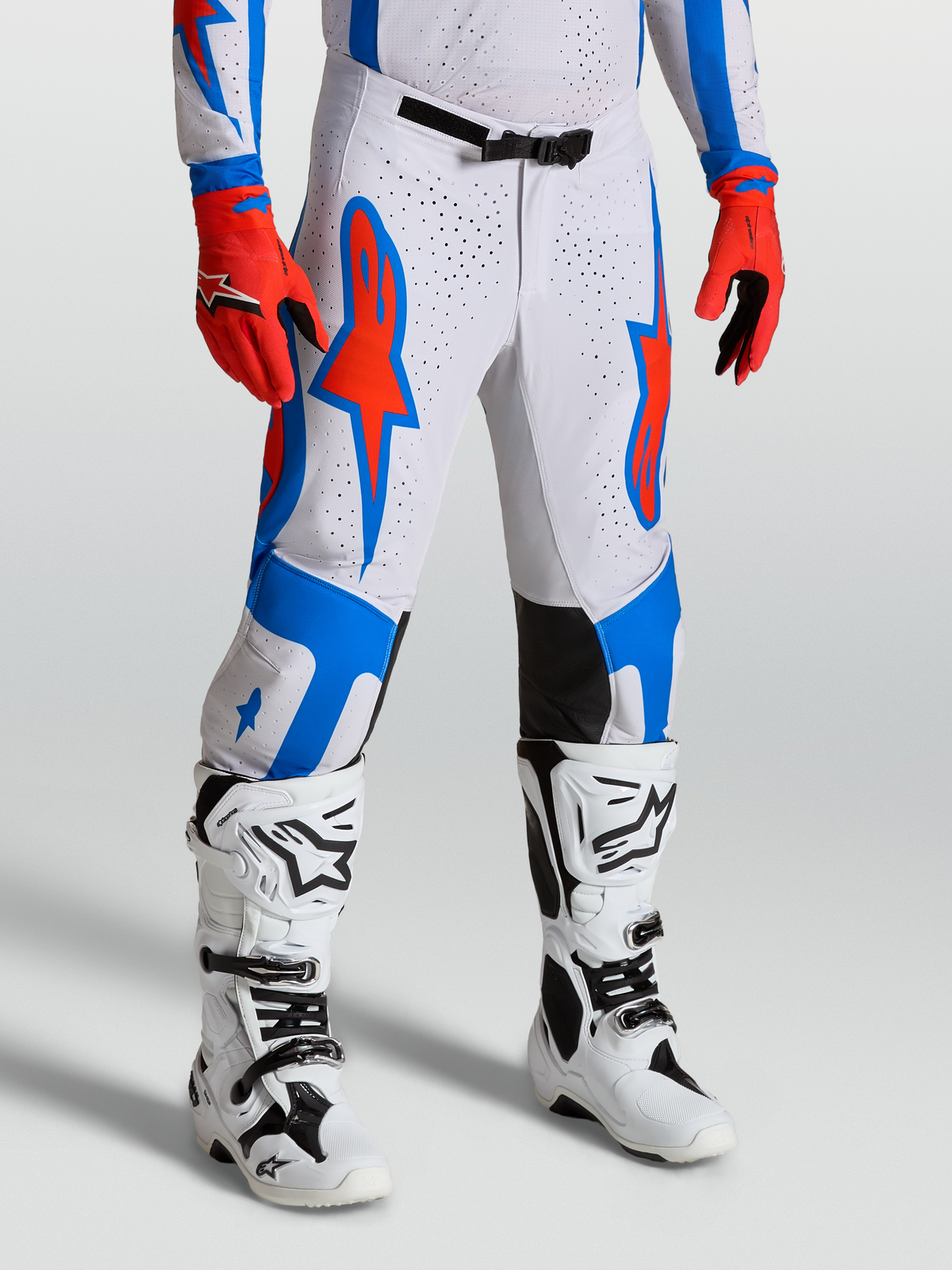 Alpinestars Pantalons Supertech Vesta, équipement de motocross blancs et rouges avec graphismes d'étoiles bleues, coupe athlétique sur mannequin.
