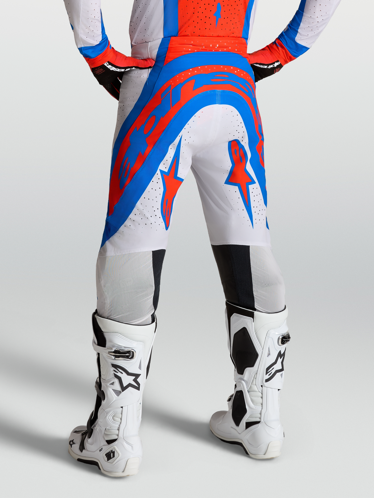 Alpinestars Pantalons Supertech Vesta, pantalon de motocross de niveau professionnel, blanc, rouge et bleu, tissu rip-stop extensible perforé, porté avec des bottes de protection blanches