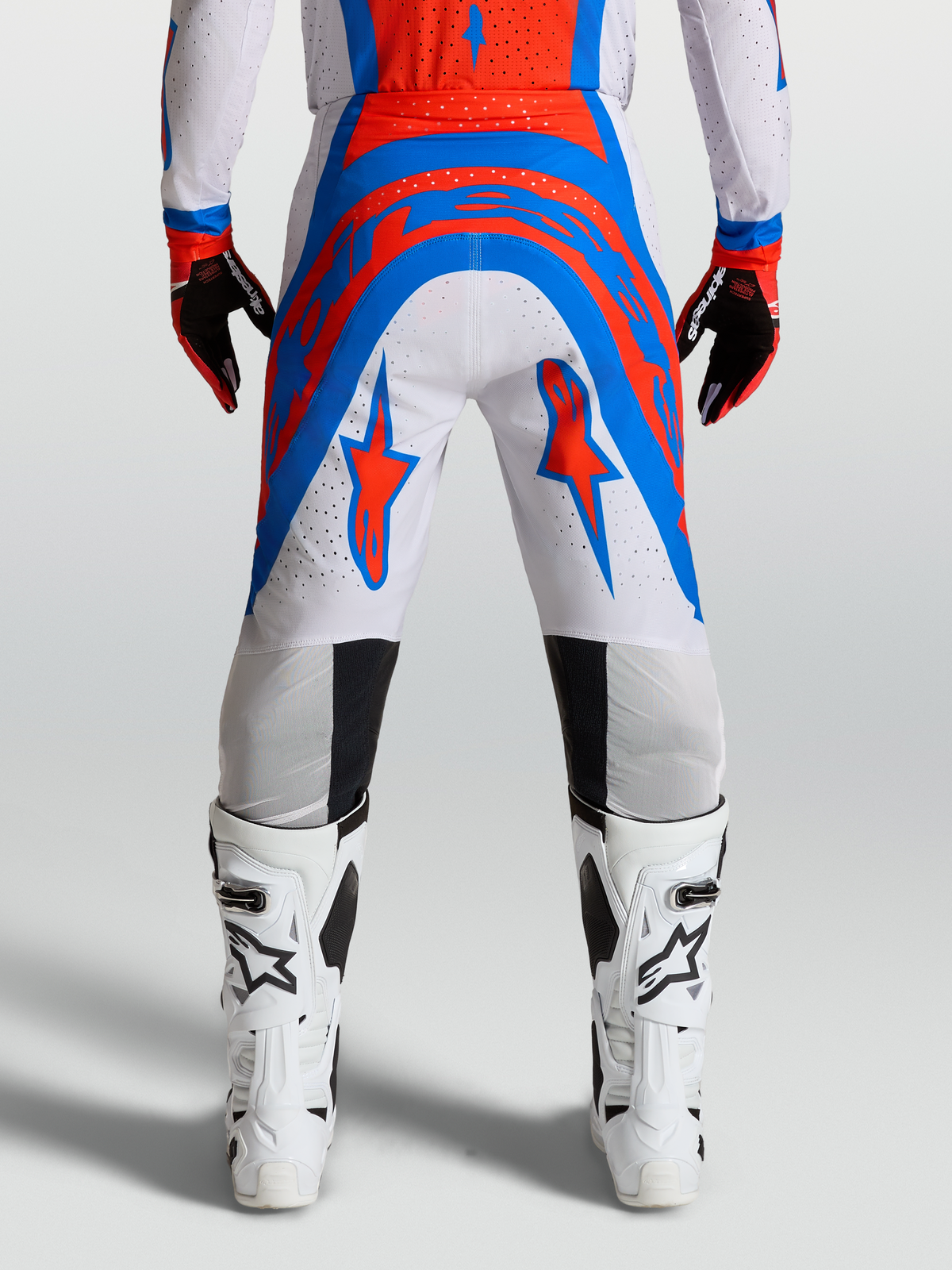 Alpinestars Pantalons Supertech Vesta, pantalon de motocross professionnel, rouge et bleu sur fond blanc, coupe athlétique performance, vue de dos sur mannequin avec bottes blanches