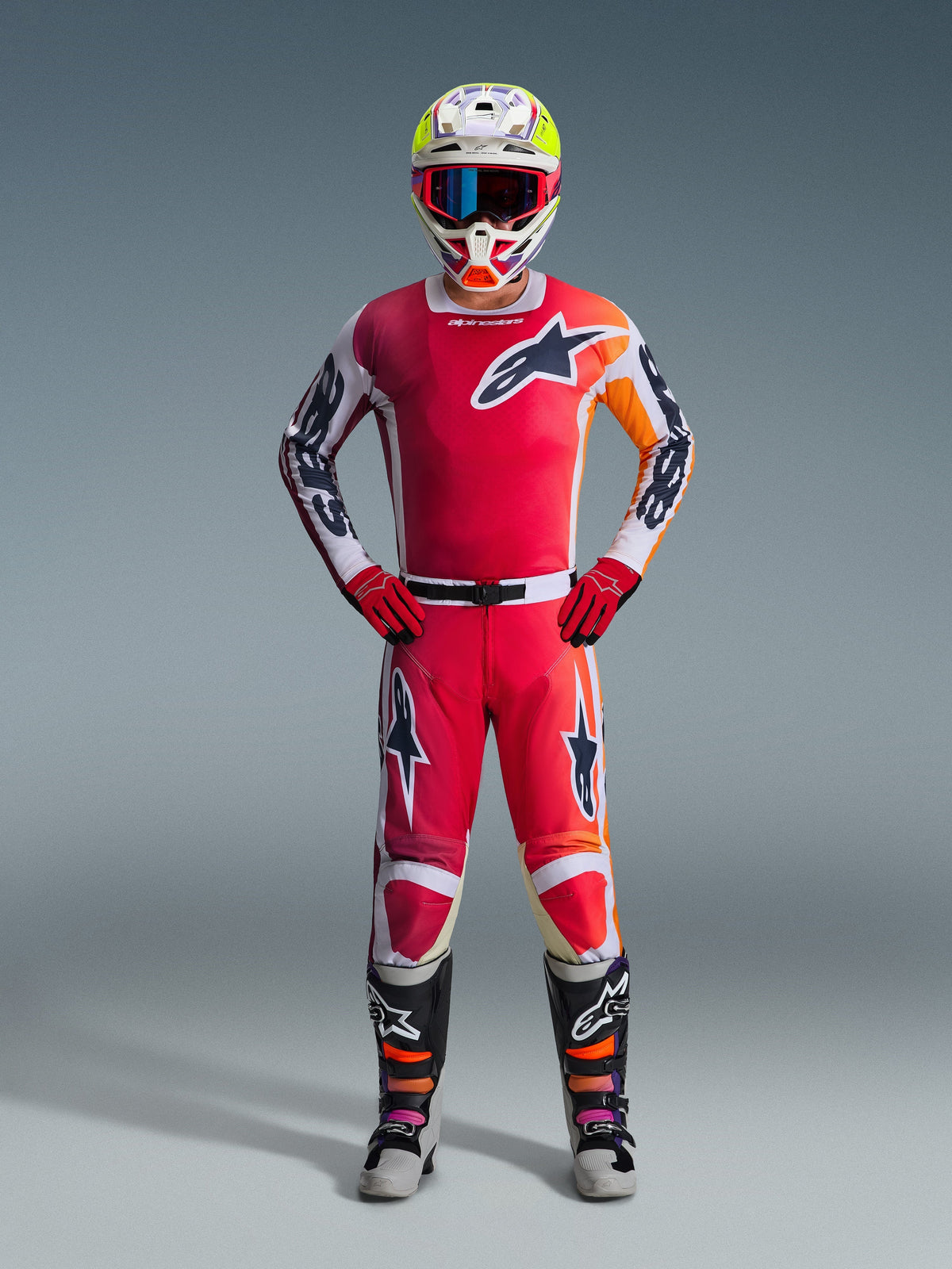 Pilote de motocross portant une tenue de course complète, maillot rouge avec des accents blancs et orange, pantalon Racer Portl 2026 en rouge et blanc, casque blanc avec des accents colorés et lunettes bleues, gants rouges et bottes noires et grises, tenue coordonnée pour la performance tout-terrain