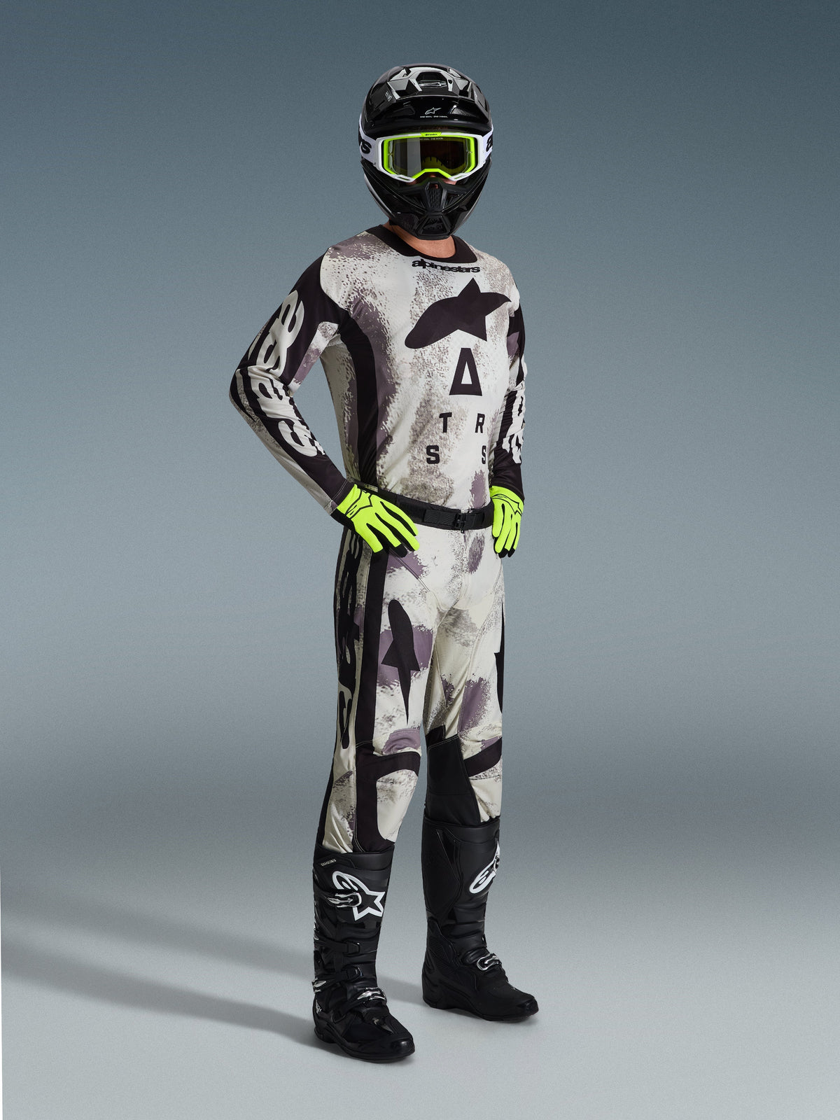 Tenue de motocross complète Alpinestars, Pantalon Racer Lahnd 2026 en Sand Camo, maillot camouflage assorti avec logo imposant, casque noir avec lunettes jaune fluo, gants vert fluo, bottes noires, tenue professionnelle coordonnée pour la performance tout-terrain