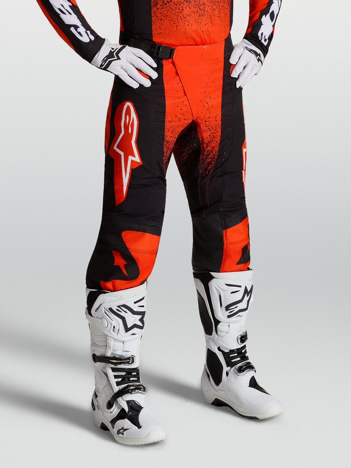 Alpinestars Techstar Swan, pantalon de motocross pour homme, rouge cardinal et noir, porté avec des bottes et des gants blancs, tissus extensibles et zone d'assise renforcée pour la course tout-terrain.