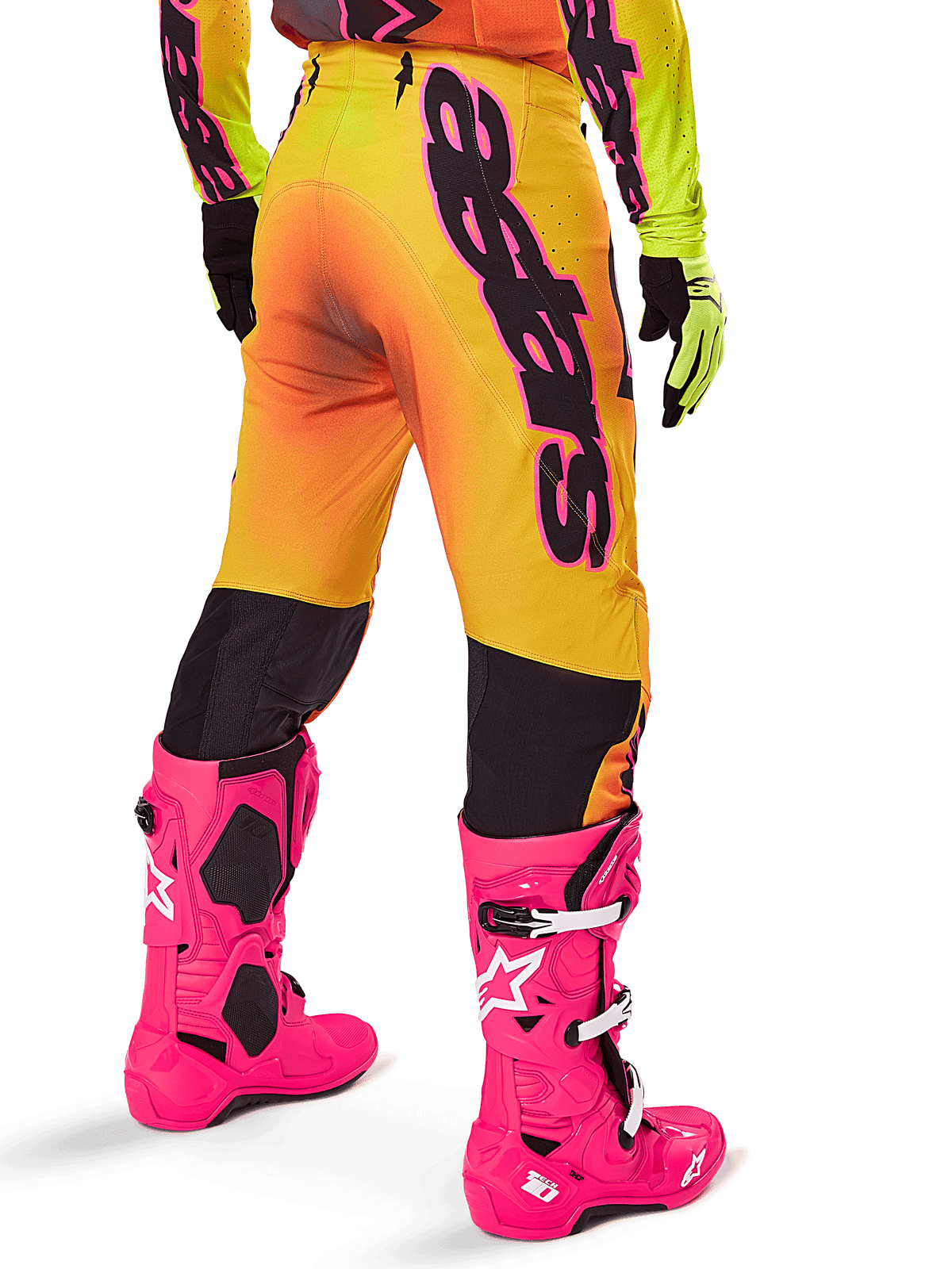 Ensemble d'équipement Alpinestars Supertech Lipan 2025, vue arrière du pantalon de motocross avec dégradé jaune et orange et marquage noir imposant, associé à des bottes Tech 10 rose vif et des gants jaunes, équipement de course tout-terrain professionnel