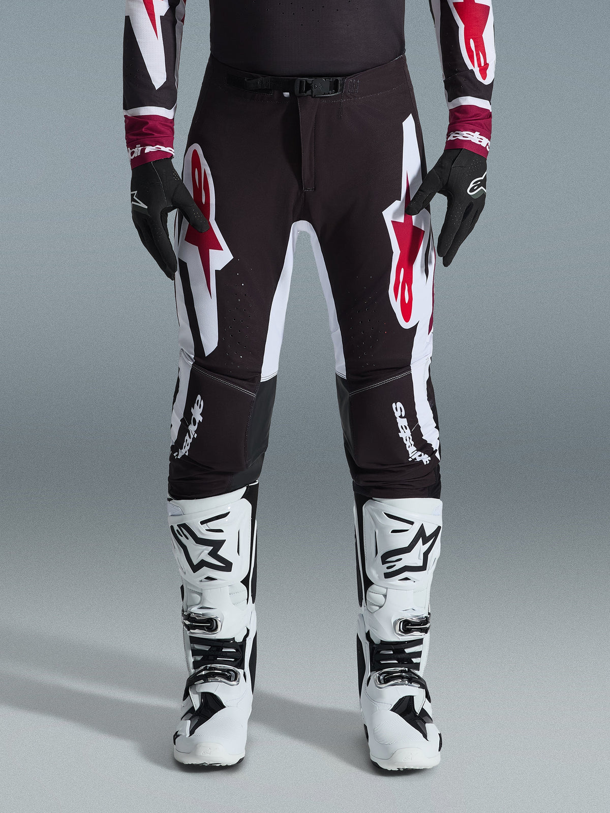 Alpinestars Supertech AFD Vista Pants 2026, pantalon de motocross, noir, rouge et blanc, avec de grands logos graphiques sur les cuisses et les genoux, porté avec des bottes de course blanches et des gants noirs, design athlétique prêt pour la compétition tout-terrain d'élite