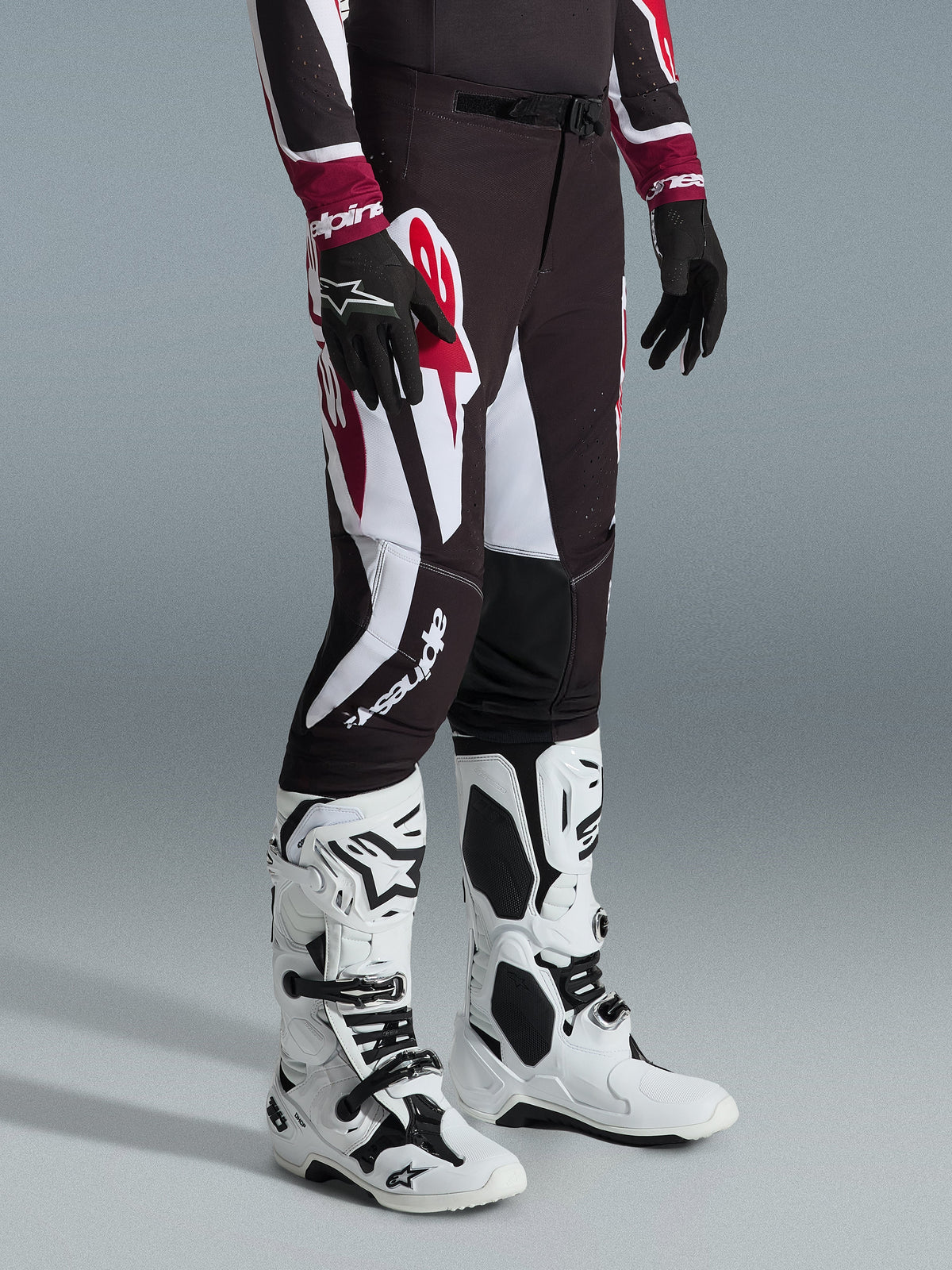 Pantalon Alpinestars 2026 Supertech AFD Vista, pantalon de motocross, noir, rouge et blanc, porté avec des bottes de motocross blanches et noires et des gants noirs, avec de larges motifs graphiques blancs et rouges, design à coupe athlétique de course