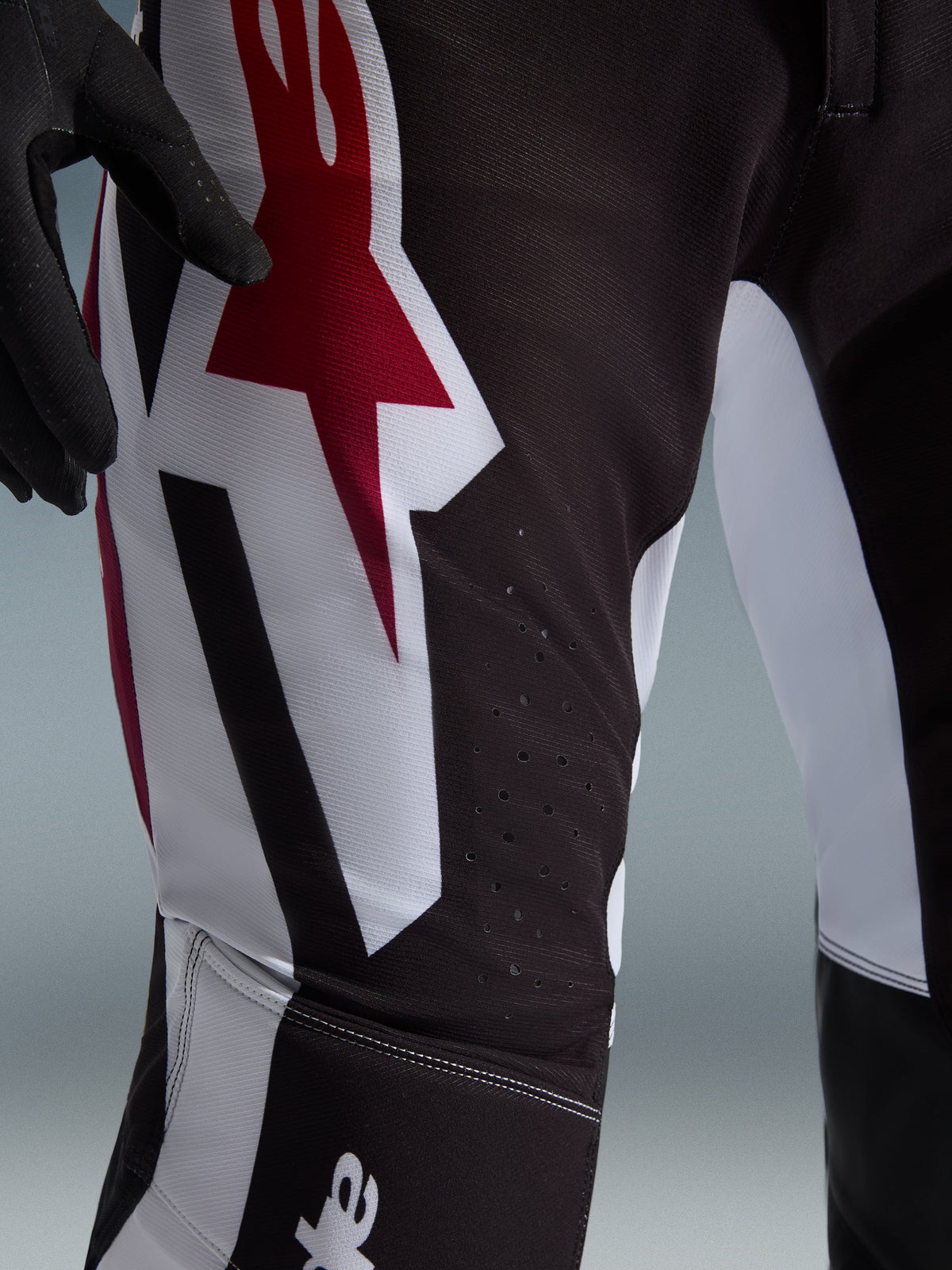 Alpinestars 2026 Supertech AFD Vista Pants, pantalon de motocross, noir, rouge et blanc, gros plan de la zone de la cuisse présentant un grand logo étoile rouge et blanc, perforations découpées au laser pour la circulation de l'air et tissu ripstop extensible durable.