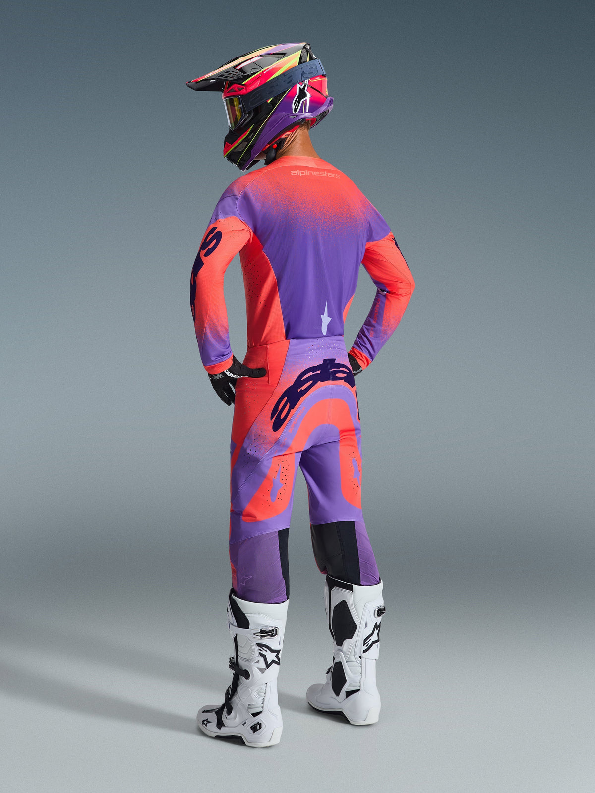 Alpinestars 2026 Supertech Scenz Pants, pantalon de motocross, Hot Coral et violet, vue arrière montrant un logo imposant sur l'assise, porté par un pilote avec un maillot assorti et des bottes blanches, équipement de course tout-terrain professionnel.