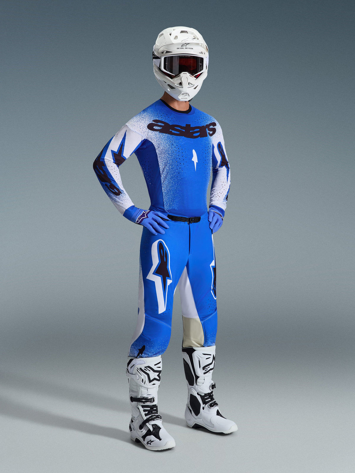 Pilote de motocross portant une tenue de course complète, comprenant le pantalon Supertech Scenz 2026 en bleu UCLA et blanc, un maillot bleu et blanc assorti avec le logo Astars, un casque blanc avec des lunettes rouges et des bottes blanches et noires, tenue coordonnée pour la course professionnelle tout-terrain.
