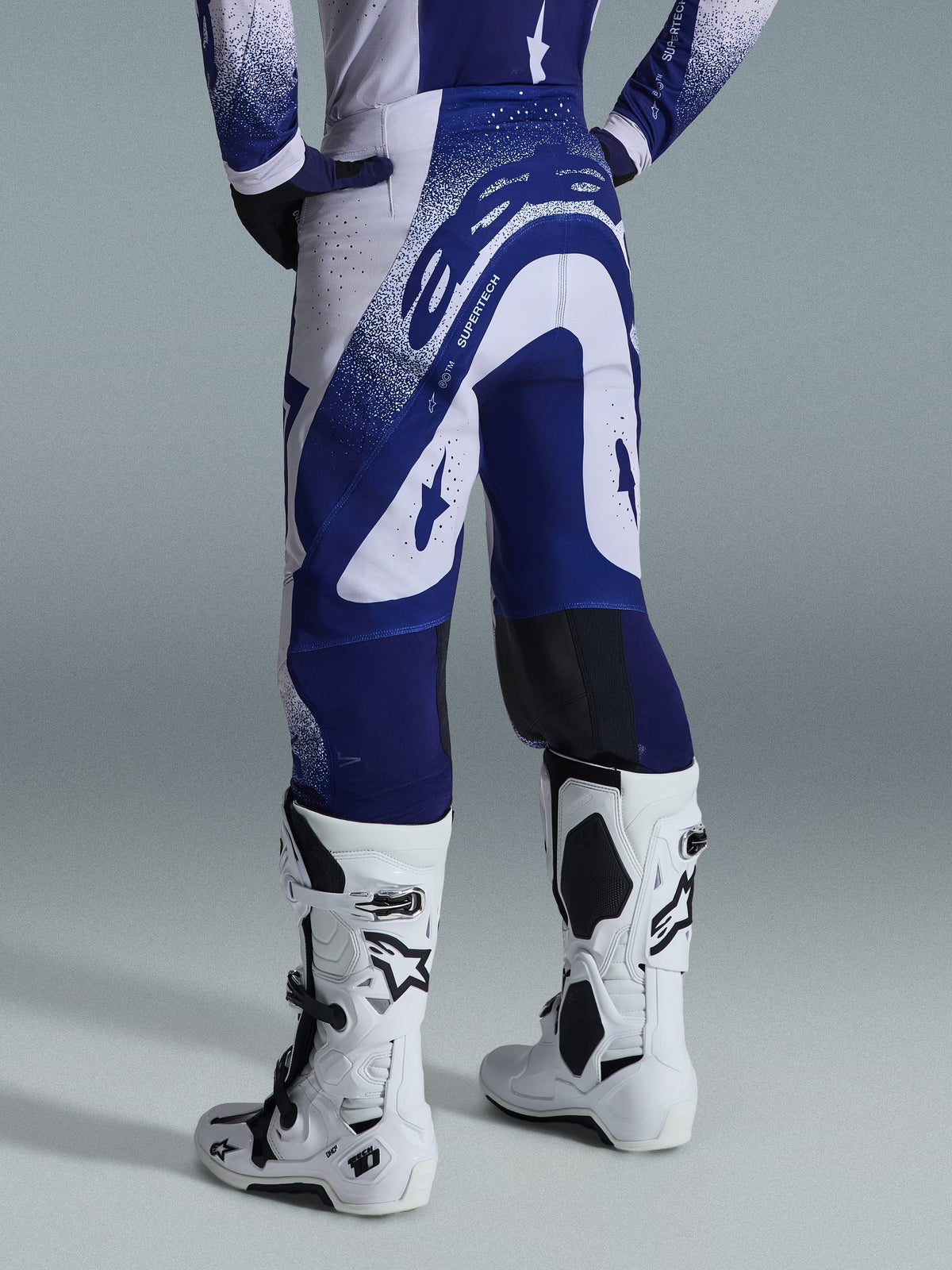 Alpinestars 2026 Supertech Scenz Pants, Motocross Pants, Light Gray and Dark Blue, rear view worn with matching jersey and white boots, featuring bold blue graphics with speckled accents, performance athletic fit for off-road racing.