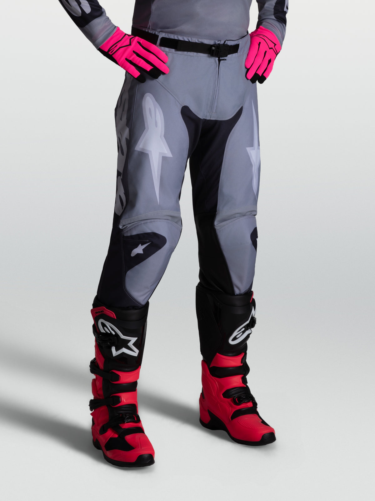 Pantalon Alpinestars Racer Amber, pantalon de motocross homme, gris et noir, en poly-tissu 600D, porté avec des bottes de protection.