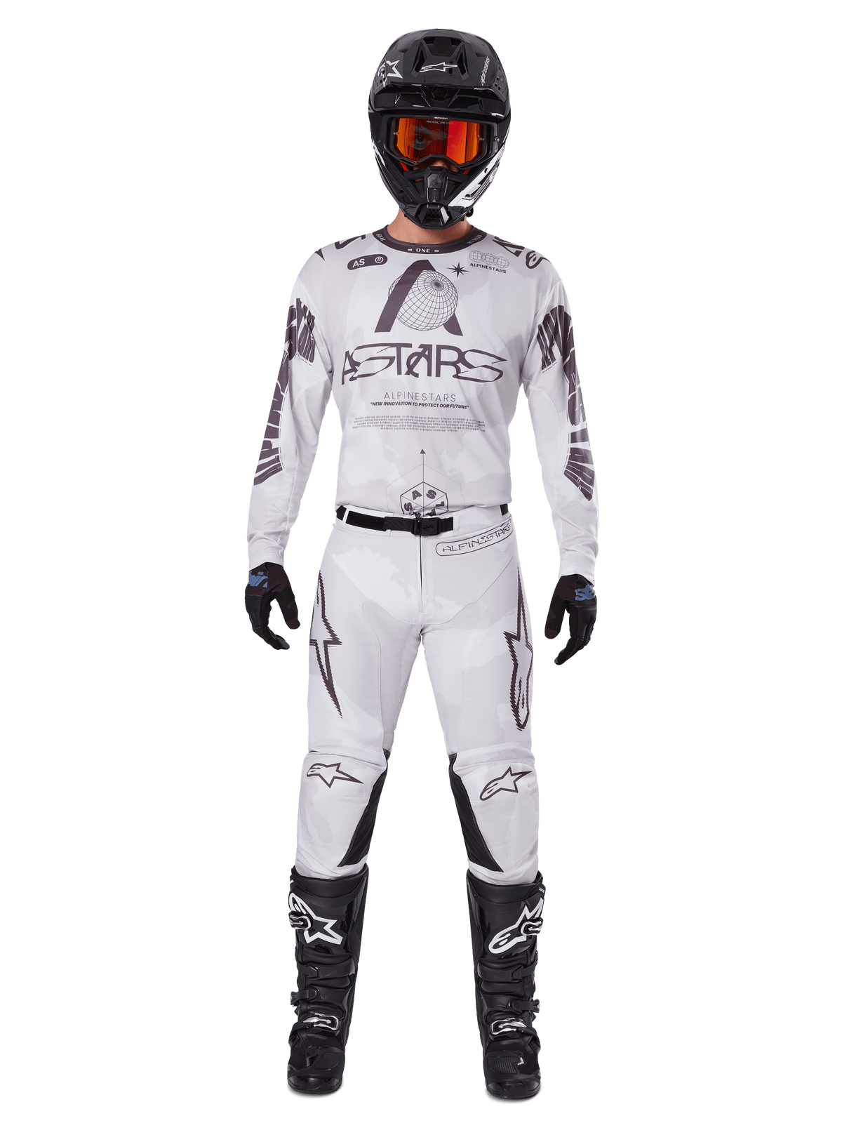 Pilote de motocross portant le pantalon Alpinestars 2025 Racer Hollow en Light Camo Brown, associé à un maillot à manches longues assorti blanc et gris, un casque noir avec lunettes orange-rouge, des gants noirs et des bottes noires, ensemble de course coordonné pour la performance tout-terrain.