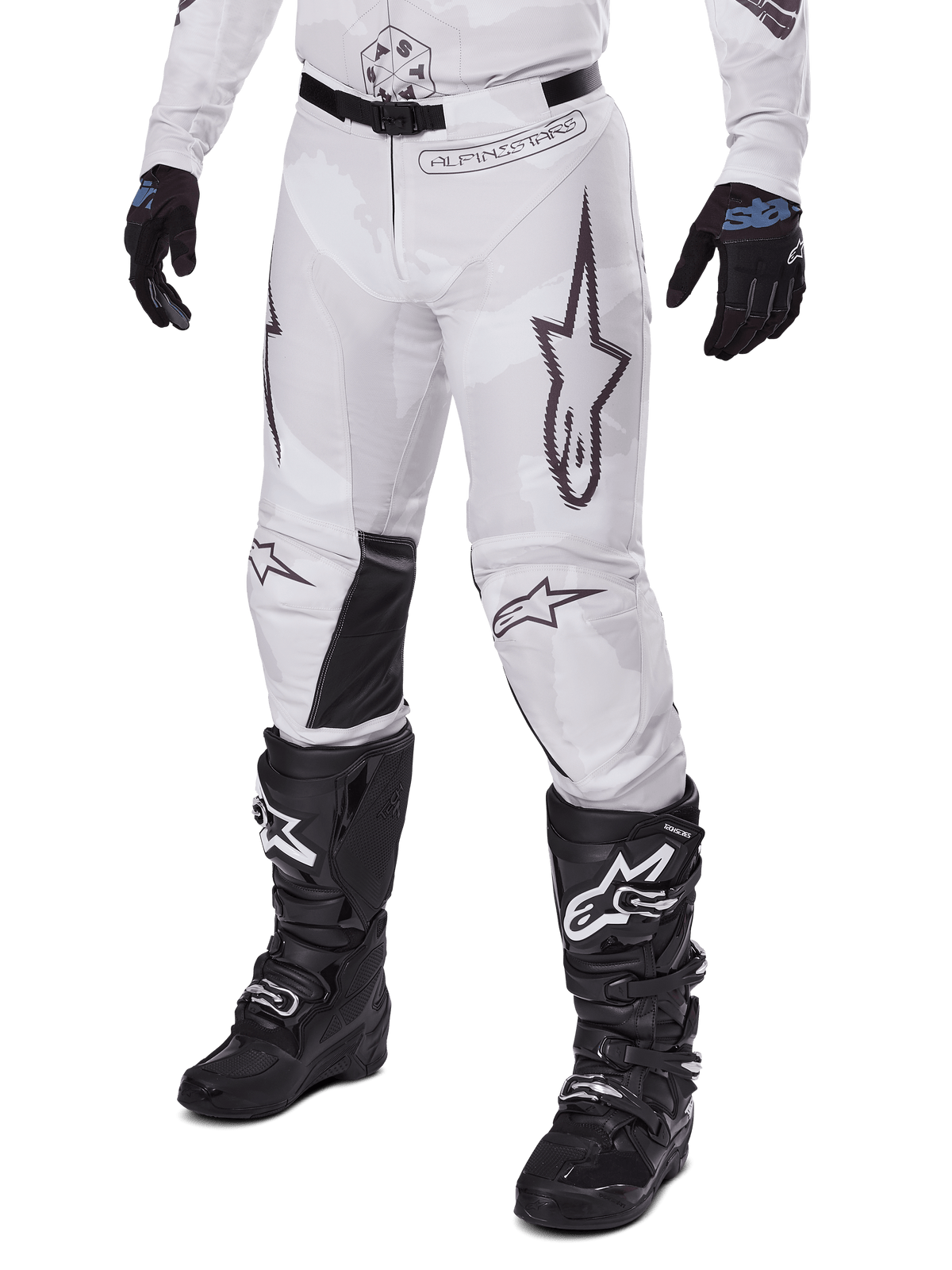 Alpinestars 2025 Racer Hollow Pants, pantalon de motocross, camouflage blanc et gris, avec de grands logos étoiles aux contours noirs et des empiècements en cuir noir à l'intérieur des genoux, porté avec des bottes et des gants de motocross noirs, conception durable pour la course tout-terrain.