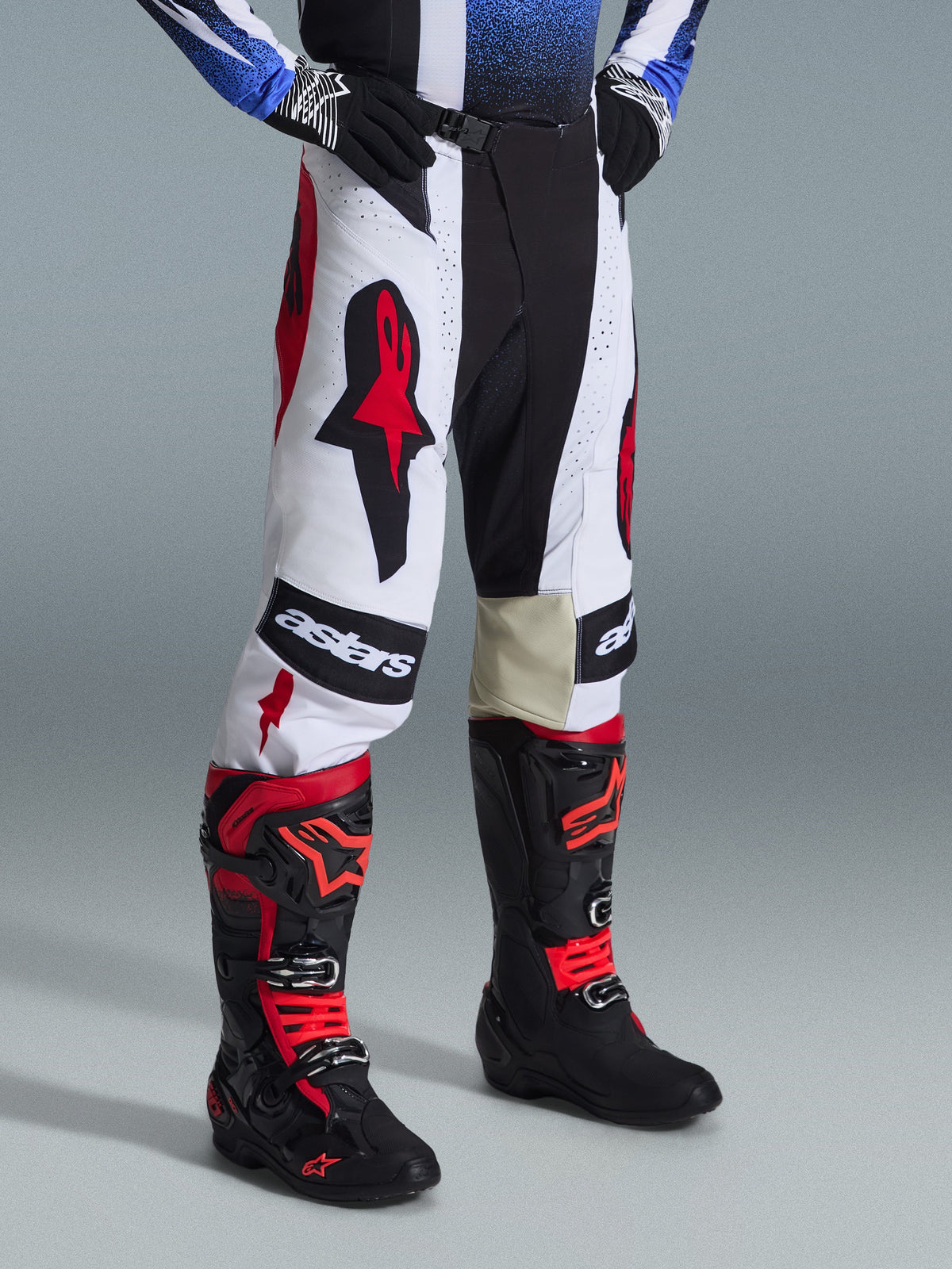 Pantalon Alpinestars Techstar Knif 2026, pantalon de motocross, noir, blanc et rouge, porté avec des bottes de motocross noires et rouges, arborant des logos Astars sur les cuisses, coupe athlétique et construction multi-panneaux durable pour le tout-terrain