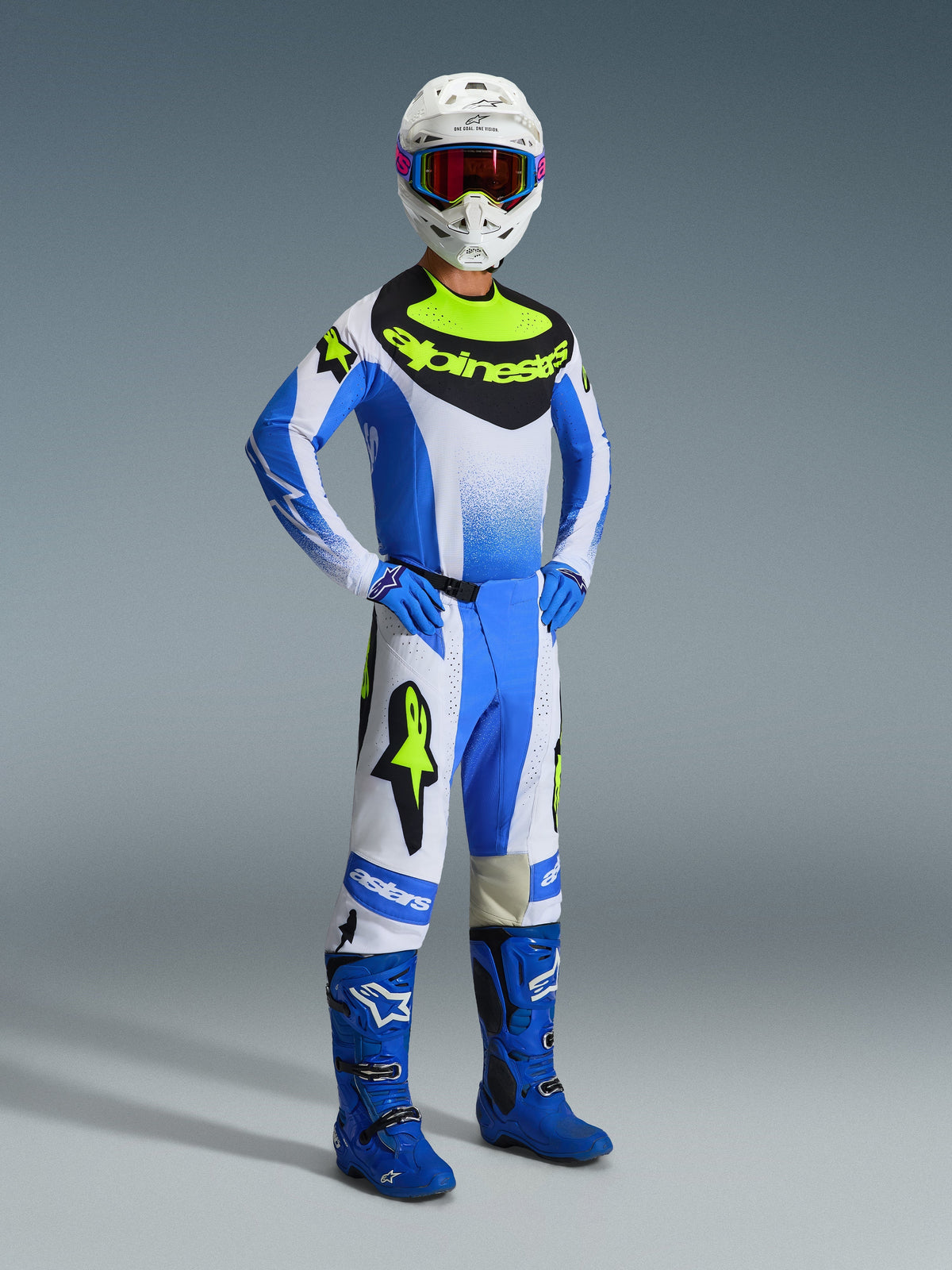 Pilote de motocross portant le pantalon Alpinestars 2026 Techstar Knif en Ucla Blue, noir et jaune fluo, tenue de course complète avec maillot assorti arborant le logo Alpinestars, bottes bleues, casque blanc avec lunettes et gants bleus, posture athlétique pour la performance tout-terrain