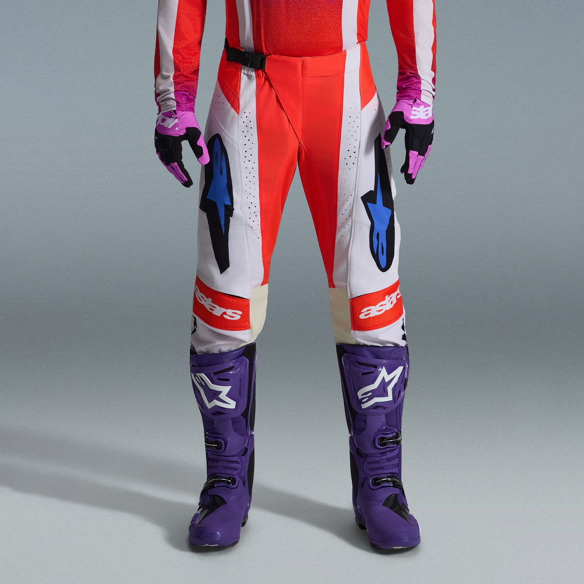 Alpinestars 2026 Techstar Knif Gear Set, lower body of motocross rider wearing red and white pants with blue accents, bright purple racing boots with white logos, and matching black and purple gloves, professional off-road racing kit