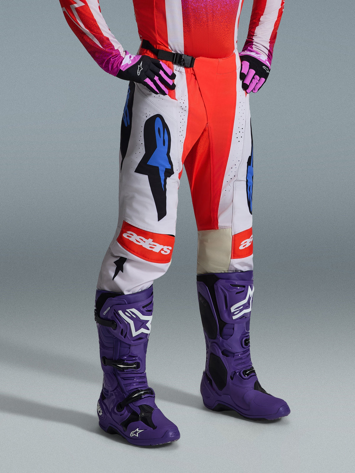 Alpinestars 2026 Techstar Knif Pants, Motocross Pants, White and Orange with Blue accents, worn as part of a complete gear set with a red and pink jersey, purple boots, and pink gloves, featuring bold logos and an athletic racing fit