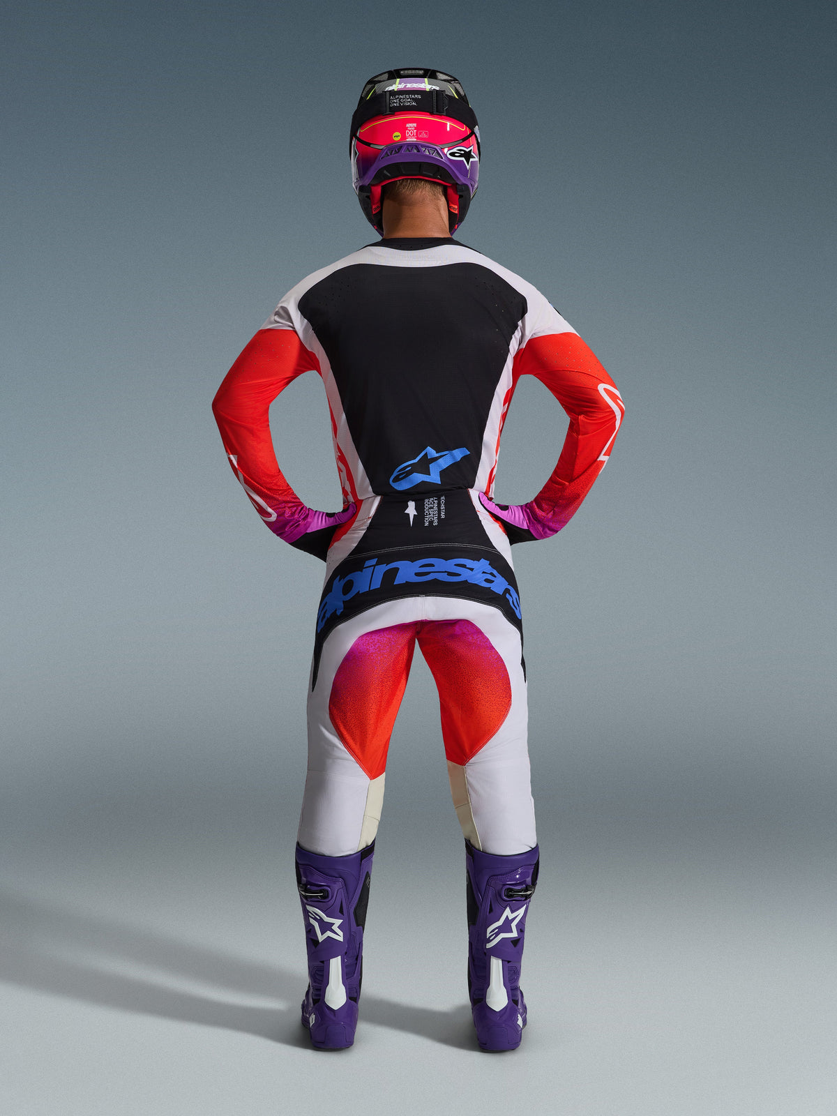 Alpinestars 2026 Techstar Knif Gear Set, complete motocross gear seen from behind, White and Black jersey with red gradient sleeves, White pants with red and pink accents, coordinated with purple boots and pink helmet, bold blue branding, professional off-road racing kit
