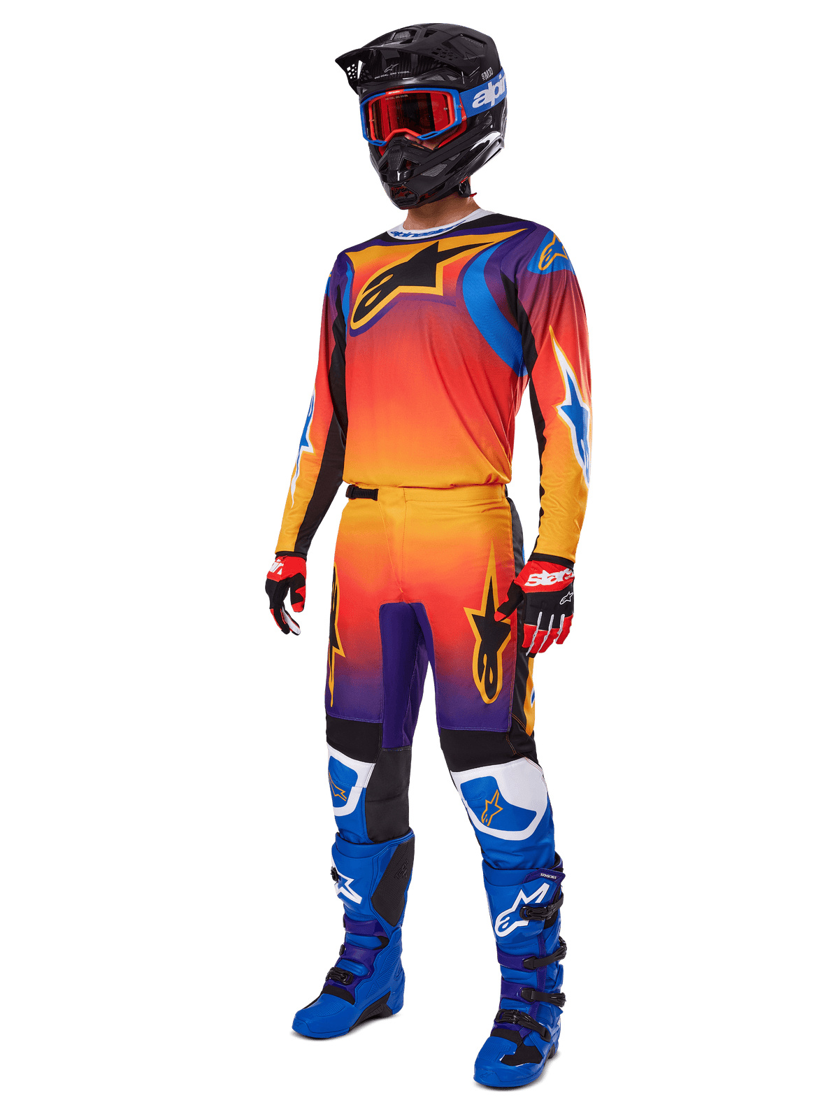 Pilote de motocross portant un équipement de course complet, pantalon Alpinestars Fluid Wurx 2025 et maillot assorti avec dégradé multicolore orange, rouge et violet, casque noir avec lunettes rouges, bottes bleues et noires, gants rouges et noirs, tenue coordonnée pour la course tout-terrain